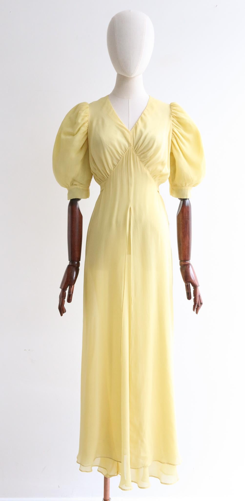 This breathtaking 1930's lemon yellow silk chiffon dress is a rare piece to behold and never again find.

Her V shaped neckline is framed by a pointed seam below the bust, gathering small pleats, that radiate across the bust line. The dress cinches