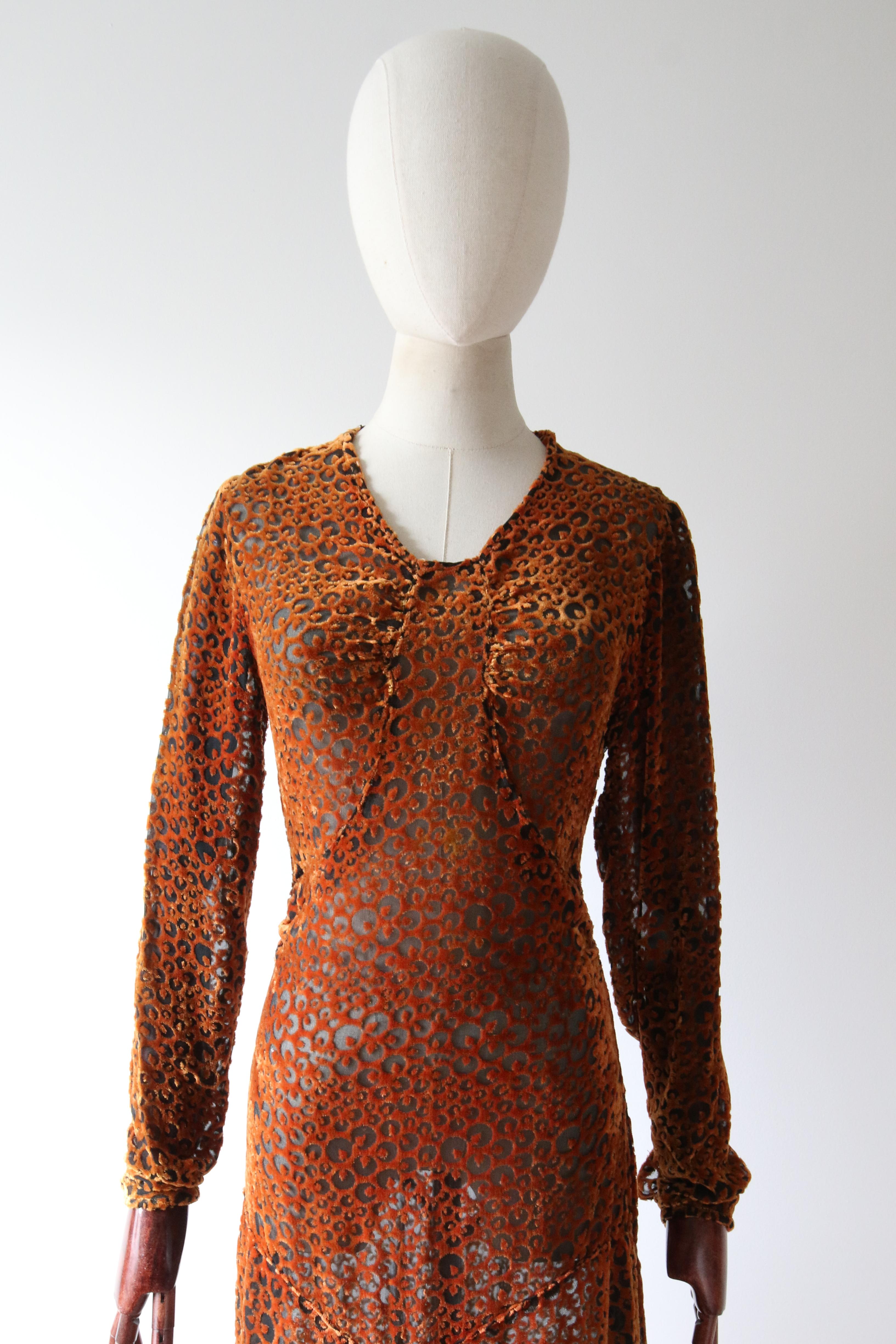 This breathtaking 1930's silk dress in a burnout devoré pattern in shades of amber and spice set against a black silk base, is a rare piece to behold. 

The rounded neckline is framed by a simple shoulder line and full length inset sleeves, edged