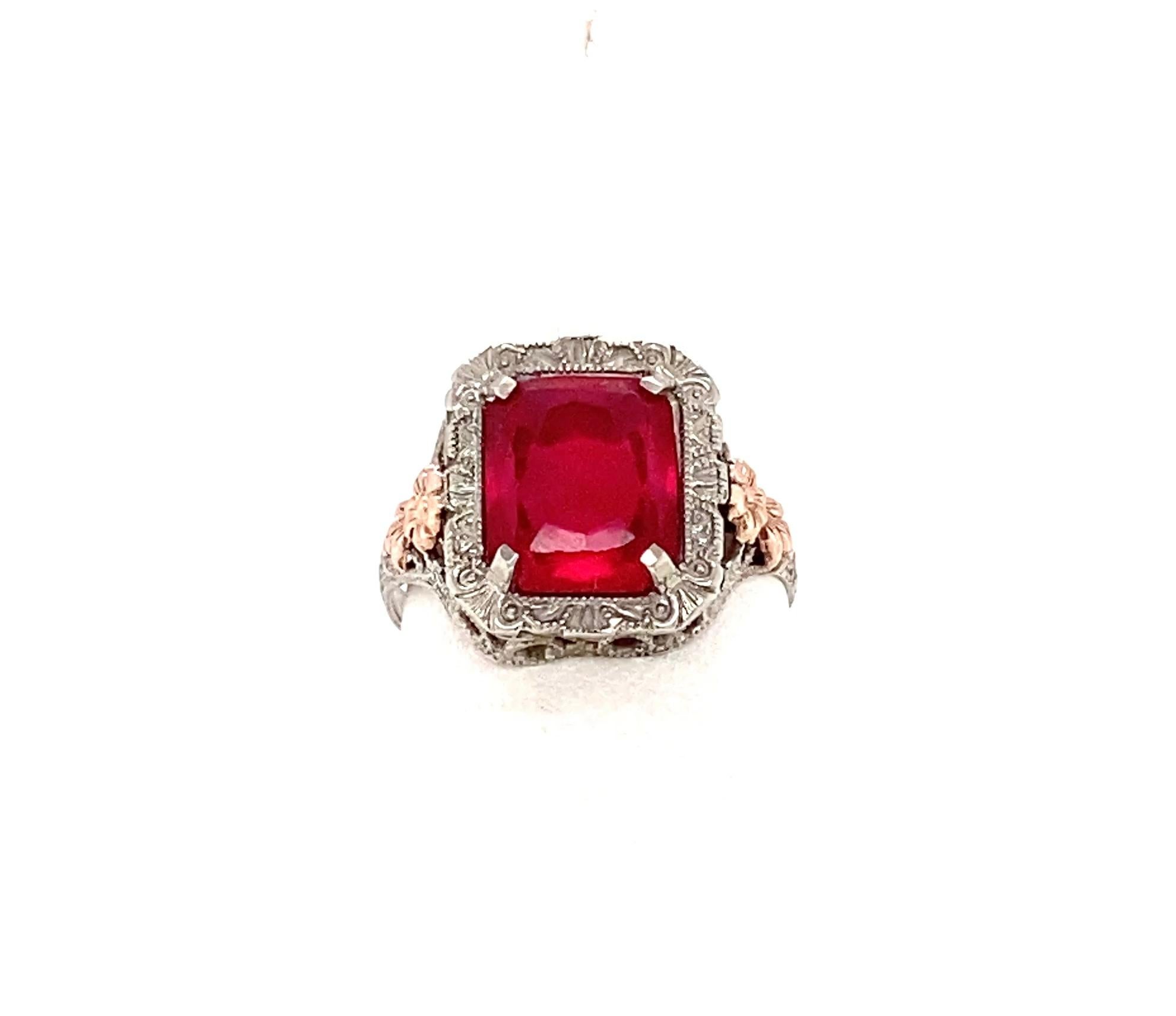 Questo incantevole anello Art Deco in oro bianco 10 carati con applicazioni in oro rosa presenta uno scintillante rubino sintetico brillante rettangolare sfaccettato di 10 mm x 8 mm, incastonato in quattro punte e circondato da un'aureola di