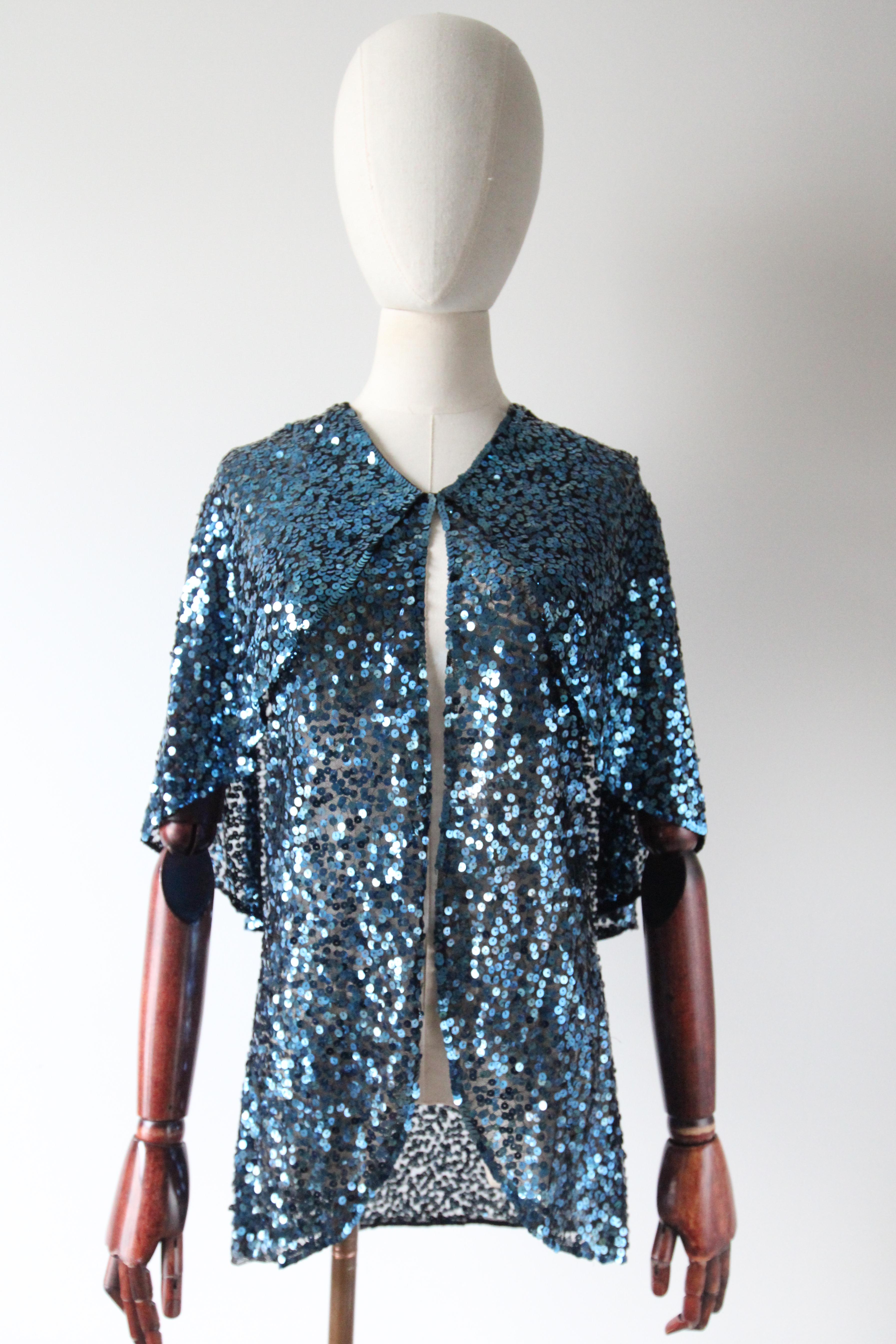 This exquisite 1930's black tulle capelet jacket, embellished with turquoise blue sequins, in a two tiered design, is a rare piece to behold and the perfect touch of sparkle to any outfit. 

The elegant V shaped neckline draws in with a concealed