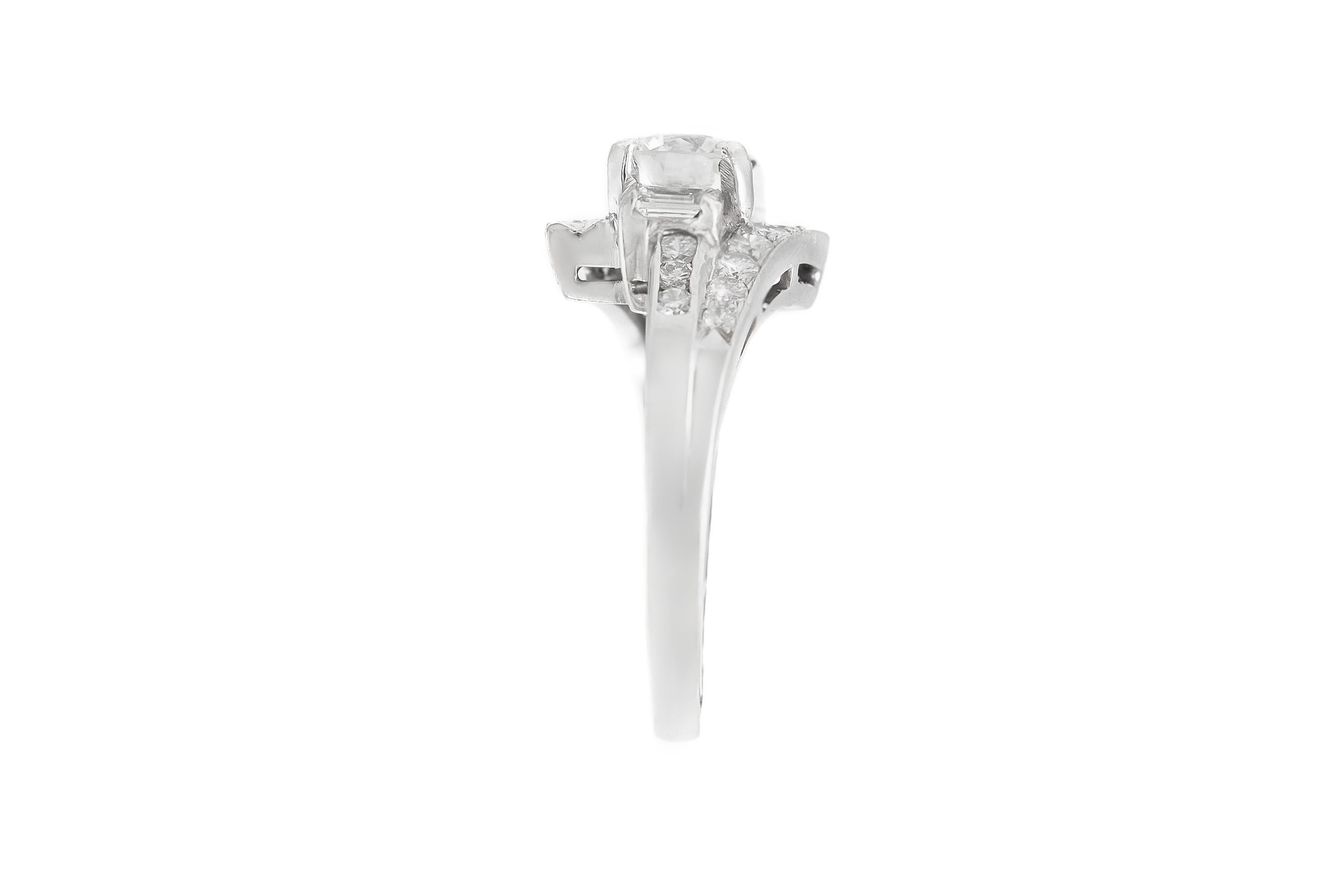 Finement réalisée en platine avec un diamant rond de taille brillant pesant environ 0,75 carat.
La bague est ornée de deux diamants latéraux de taille baguette et de diamants ronds de taille brillante sur la monture, pour un poids total d'environ
