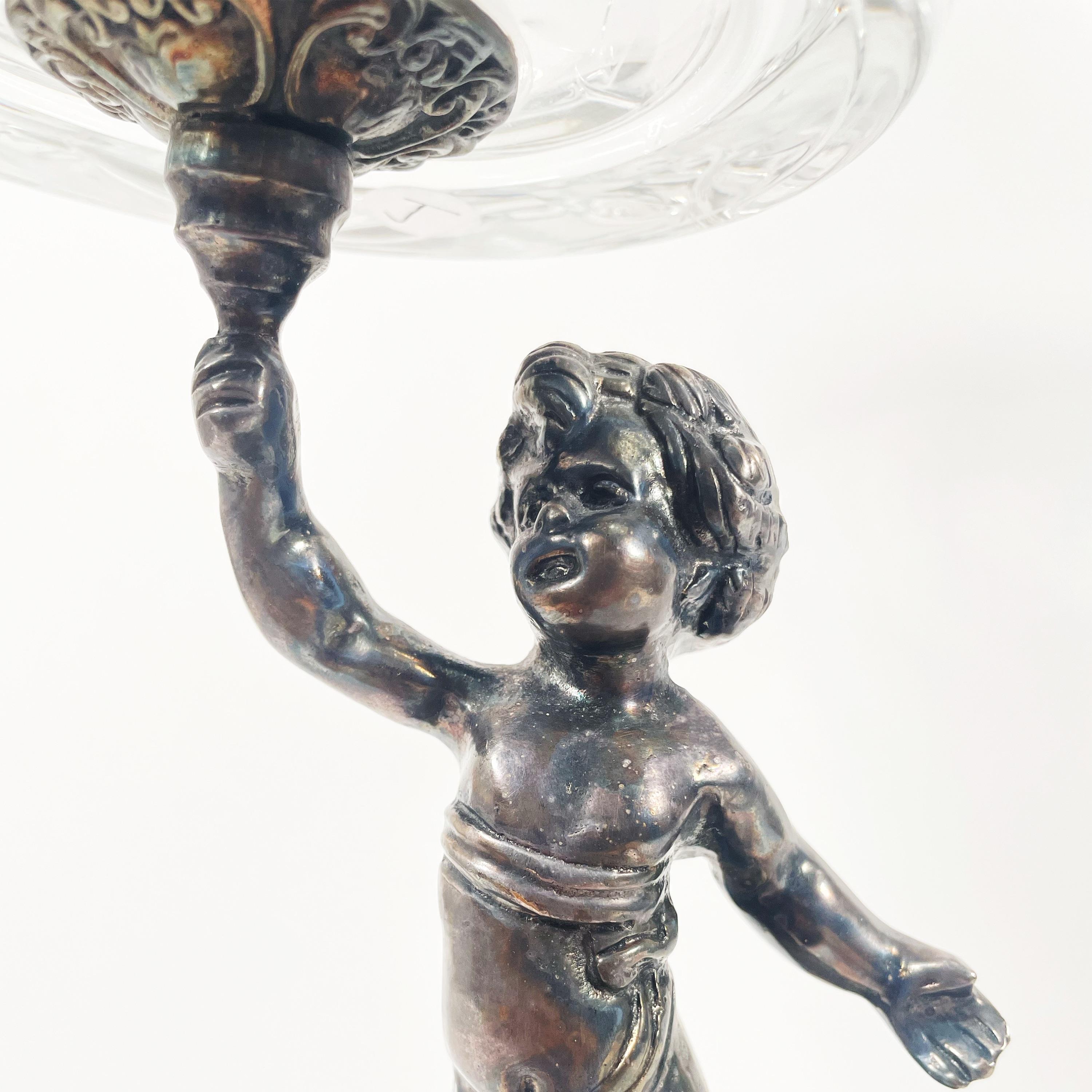 Questo squisito pezzo, un reperto vintage degli anni '40-'50, presenta una ciotola con piedistallo in cristallo tagliato e una scultura di bronzo a forma di cherubino che funge da base. Originaria dell'Inghilterra, questa incantevole ciotola con