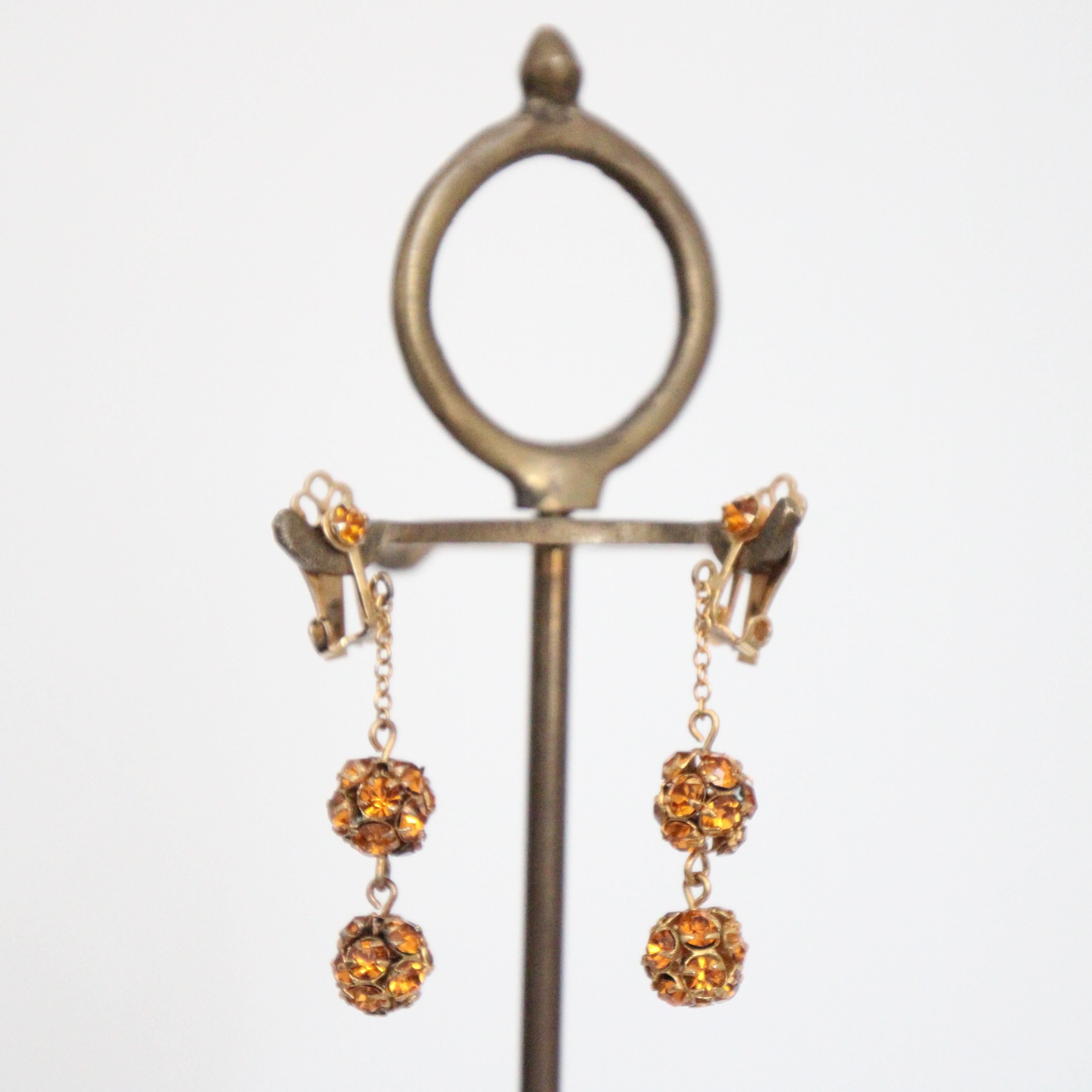 Este brillante par de pendientes de clip de los años 40, realizados en metal dorado con brillantes de cristal de color ámbar, son el toque final perfecto para tu atuendo. Los engastes de brillantes engastados en una sola garra resaltan la cadena de
