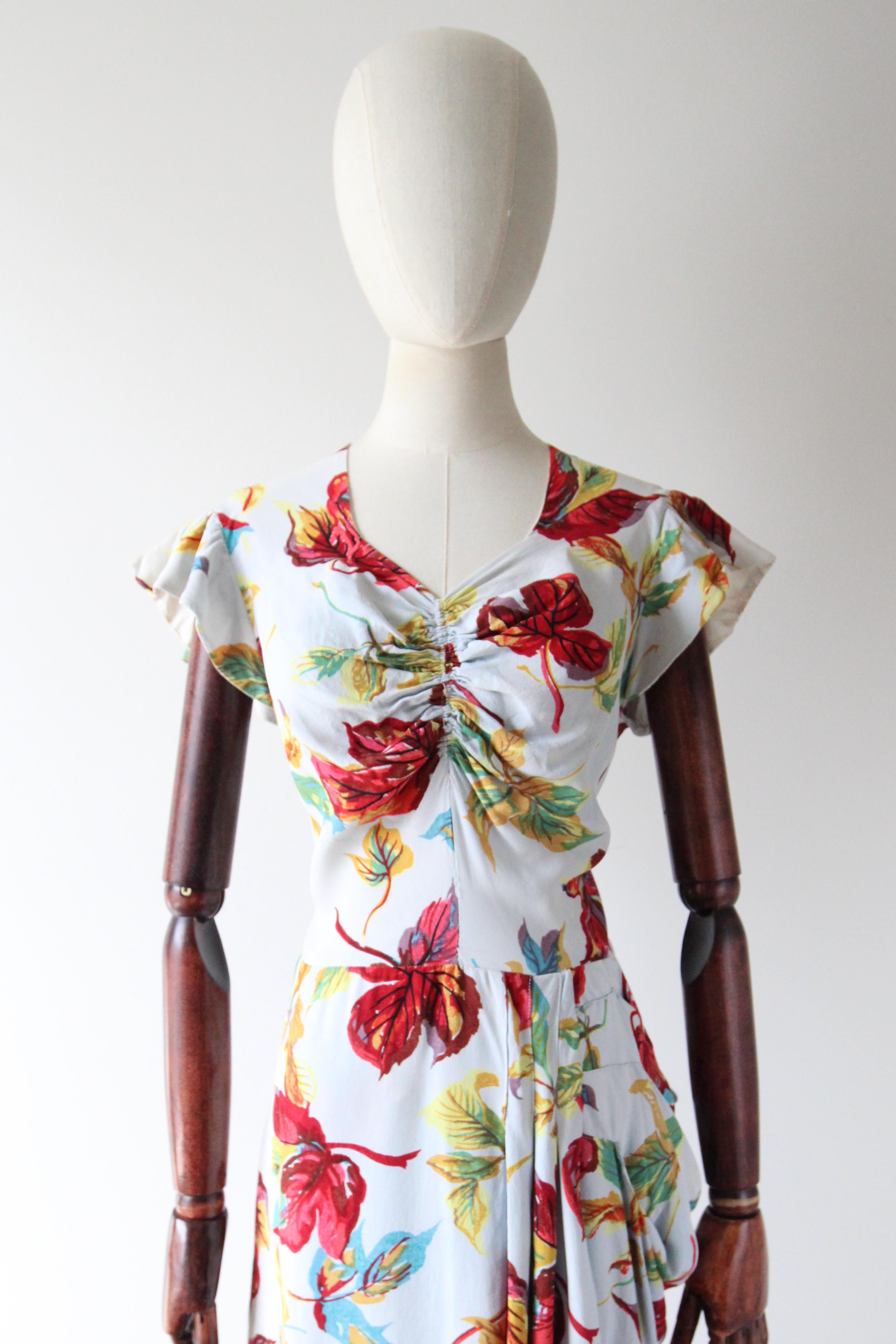 This truly enchanting 1940's crepe silk dress, rendered in a soft crepe silk with a pattern of fallen leaves in shades of red, burgundy, yellow, green, lilac and mustard, set against a pale blue background, is the perfect piece for your vintage