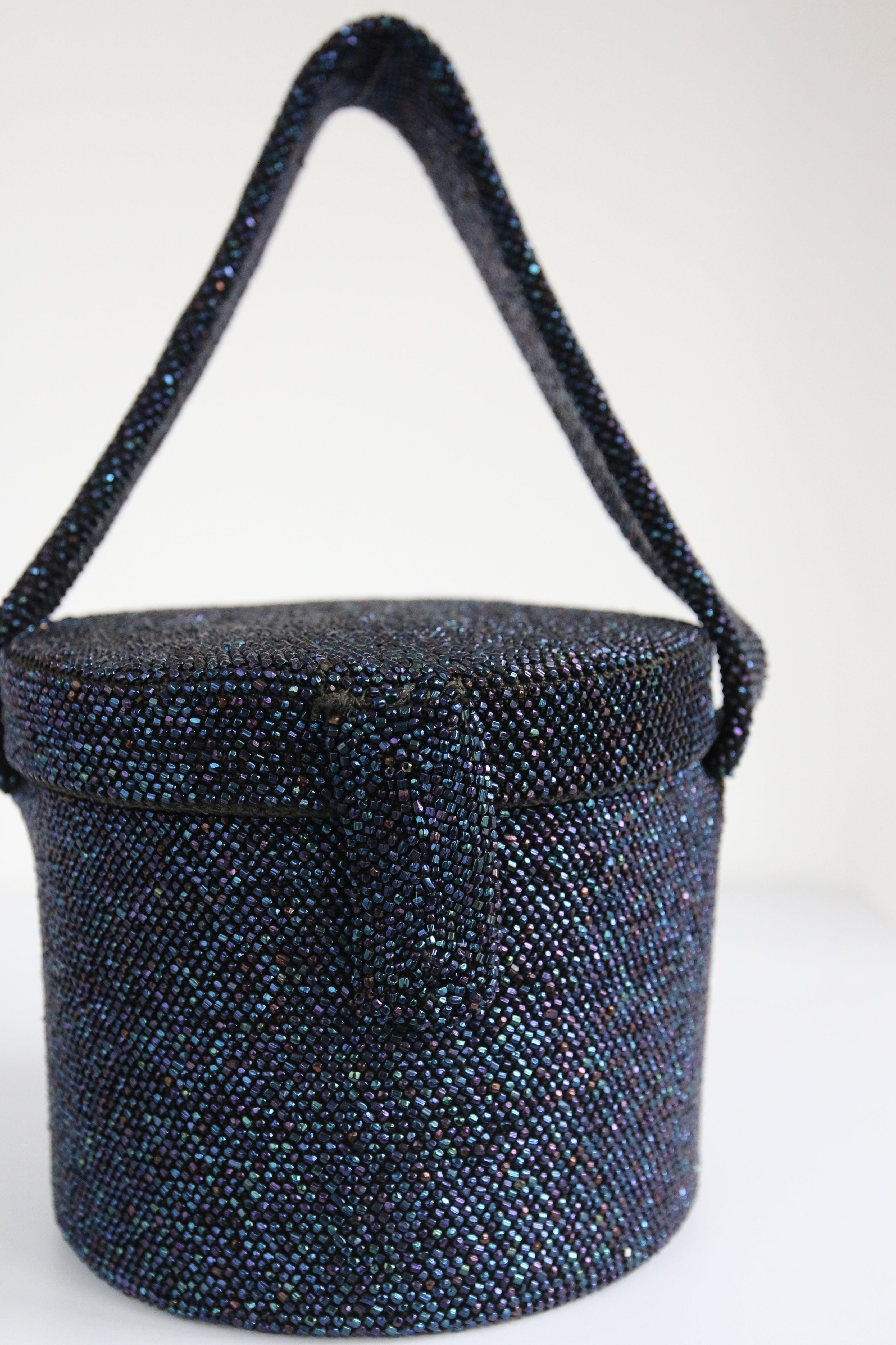 This breathtaking 1940's midnight blue bucket box bag, is the perfect finishing piece to your ensemble. 

The round bucket shape of the bag, boasts an exterior of iridescent navy blue glass faceted beads woven on a knotted cotton base, set off by a