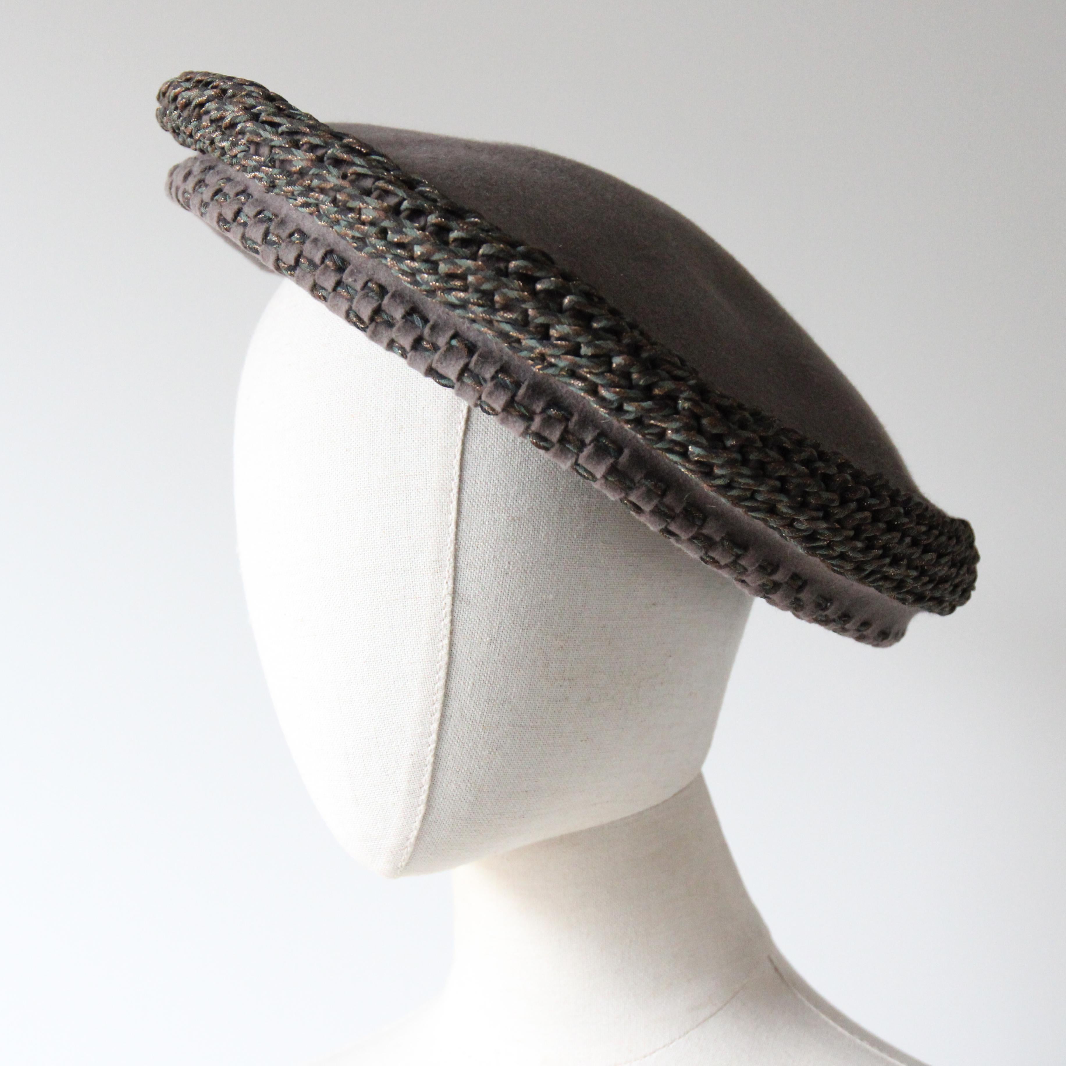 Questo raro e decadente cappello a tam in feltro di lana degli anni '40, in una classica tonalità di feltro di pelliccia grigio, arricchito da intrecci in lamé blu e oro, è il tocco finale perfetto per il tuo guardaroba stagionale. 

L'iconico stile