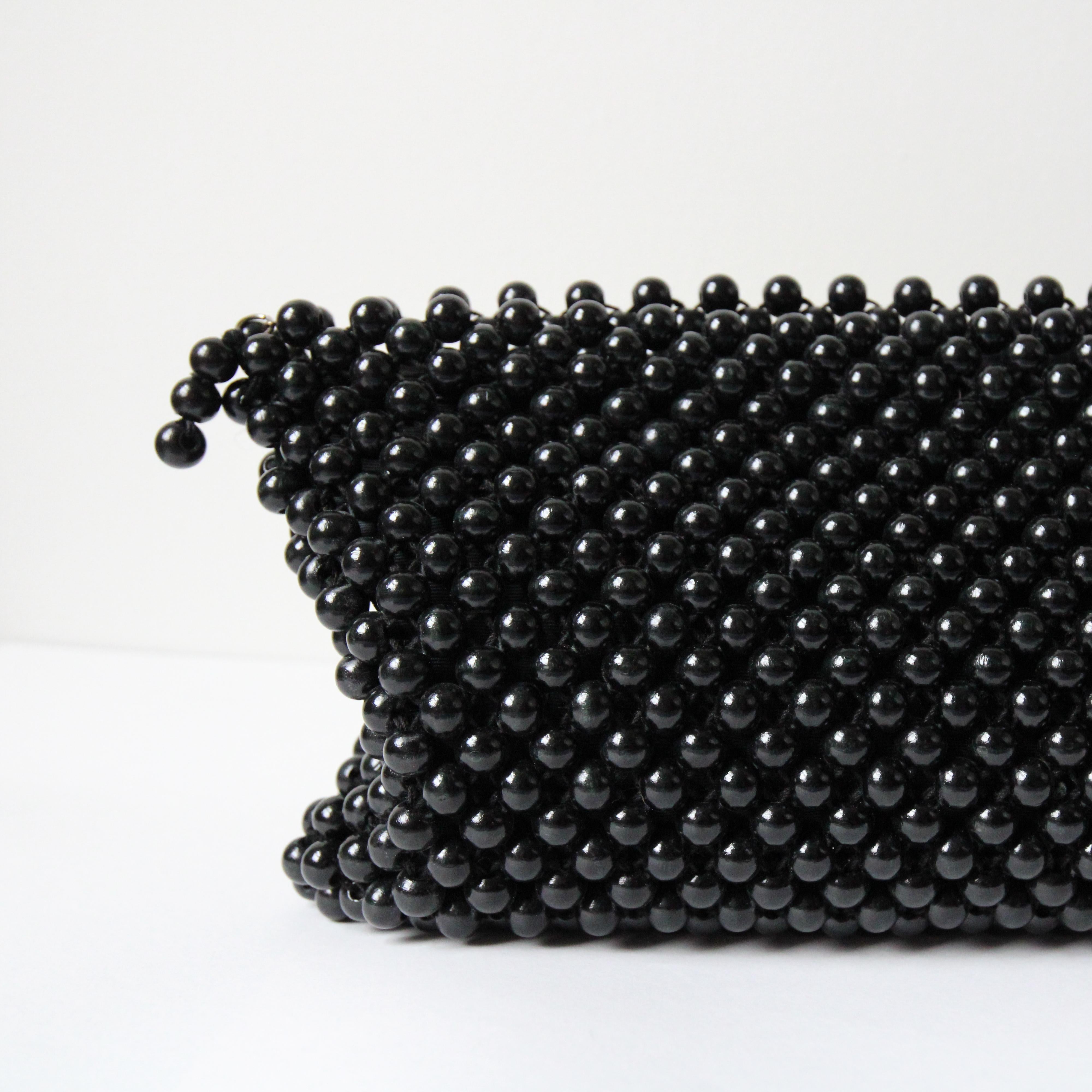 This beautiful 1940’s clutch bag, made up of knotted and woven wooden beads, painted in a deep black satin finish, above a black rayon lining, is the perfect statement accessory.  

The rectangular shape of the bag opens with a metal zip fastening