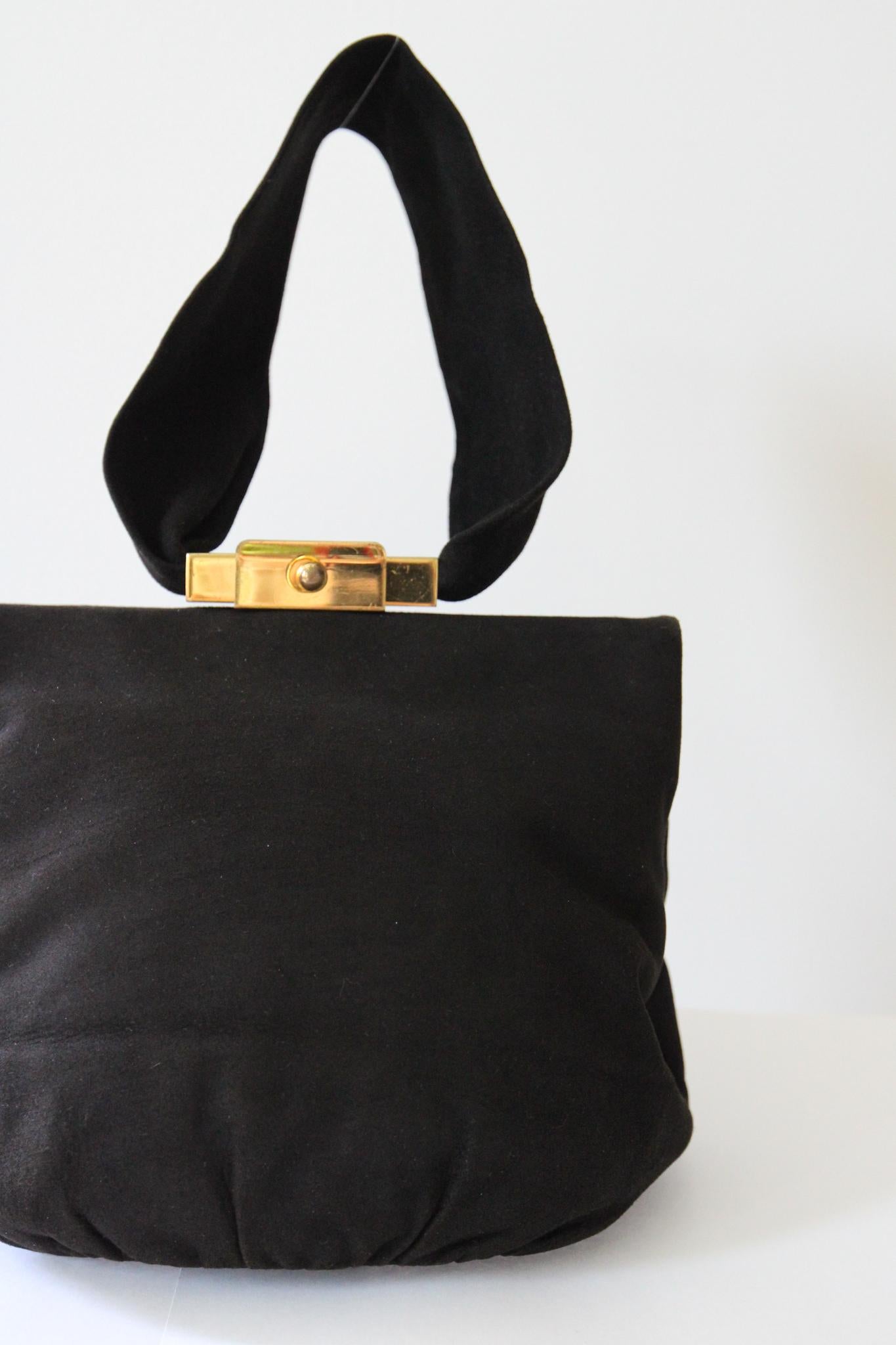 Rendered in the softest of black suedes and set off by gold toned metal hardware, this original 1940's handbag is just the perfect timeless accessory. 

The straight cut of the concealed metal frame, is accented by a statement gold toned metal push