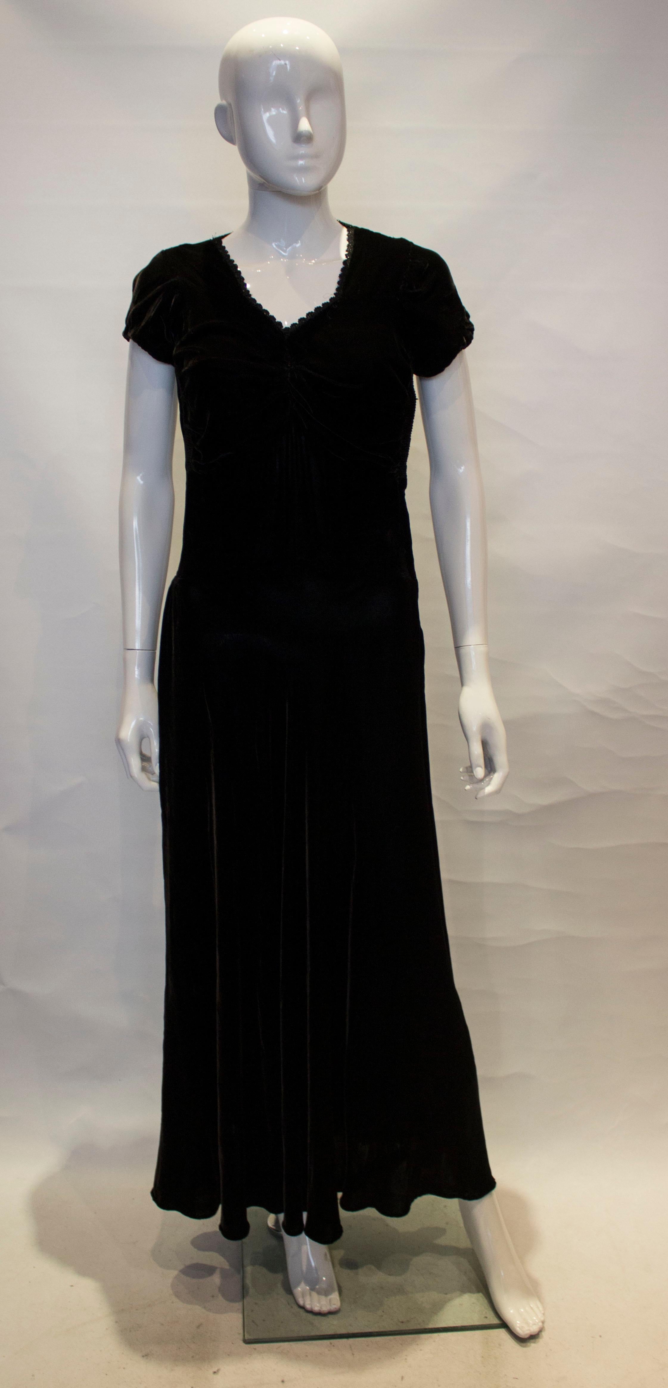  Un impresionante vestido vintage de terciopelo negro. El vestido tiene escote corazón, con fruncidos en el pecho y en la costura lateral. Tiene mangas casquillo y cremallera lateral.