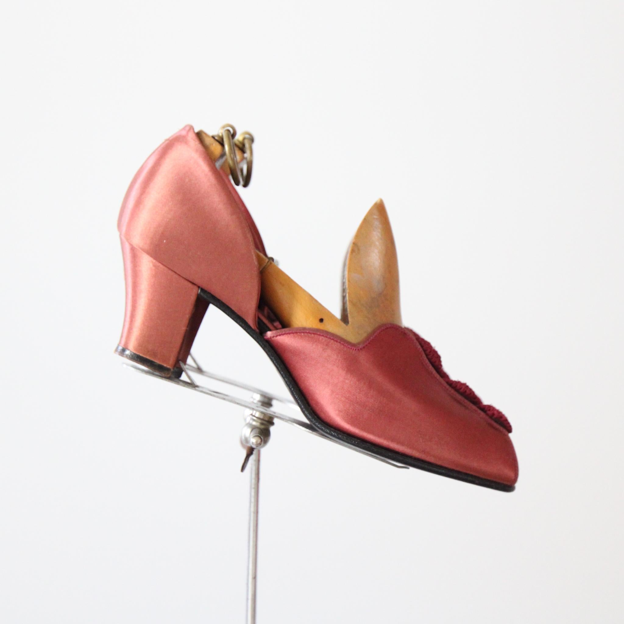 La plus belle paire de pantoufles de boudoir des années 1940 que vous puissiez espérer voir. Réalisée dans une chaude nuance de satin rose blush et rehaussée de rosettes festonnées en rayonne bordeaux, cette paire originale de pantoufles Daniel