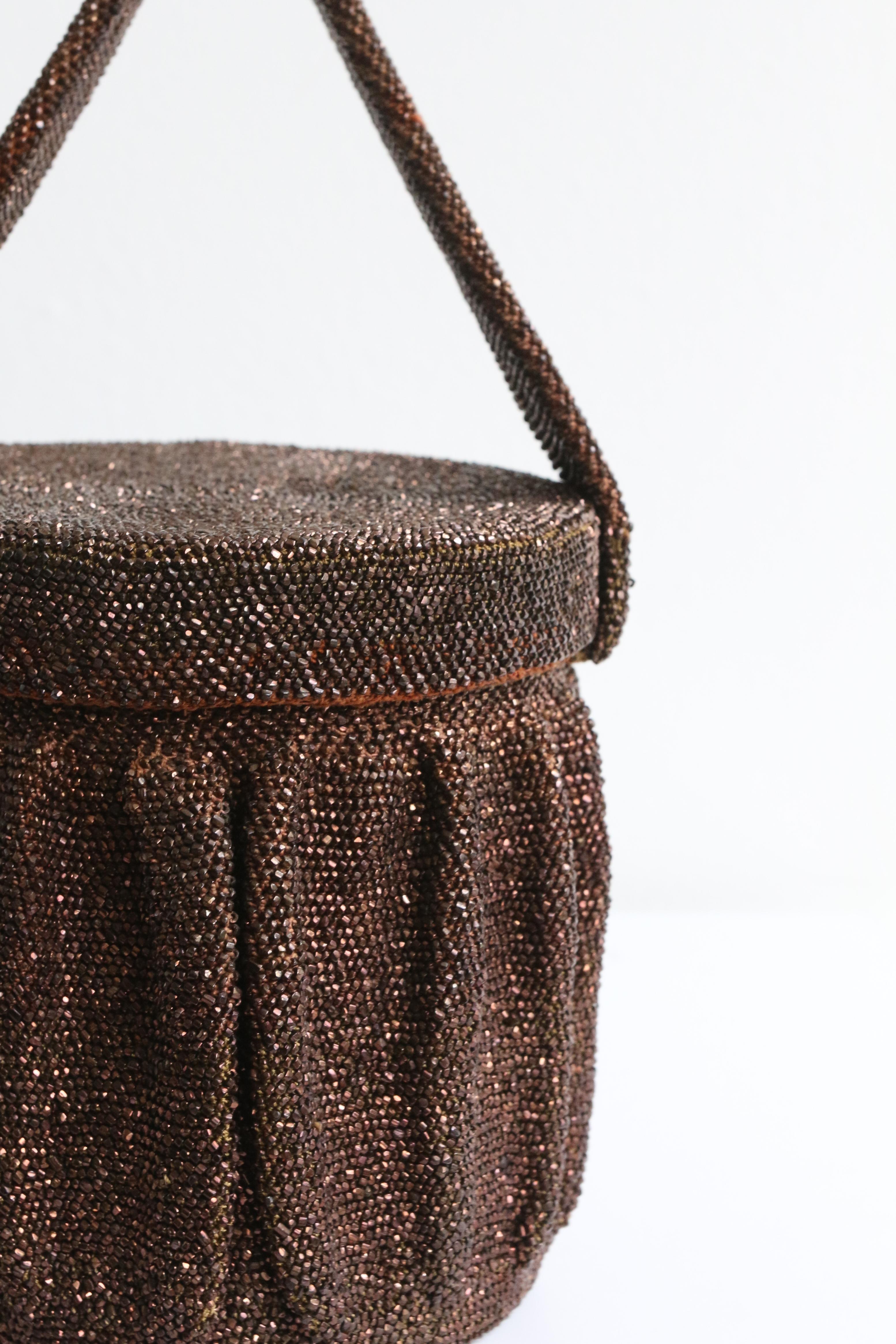 This breathtaking 1940's bucket box bag, is the perfect finishing piece to your ensemble. 

The bucket shape of the bag, boasts an exterior of bronze glass faceted beads woven on a knotted cotton base, set off by pleated details and a wonderful