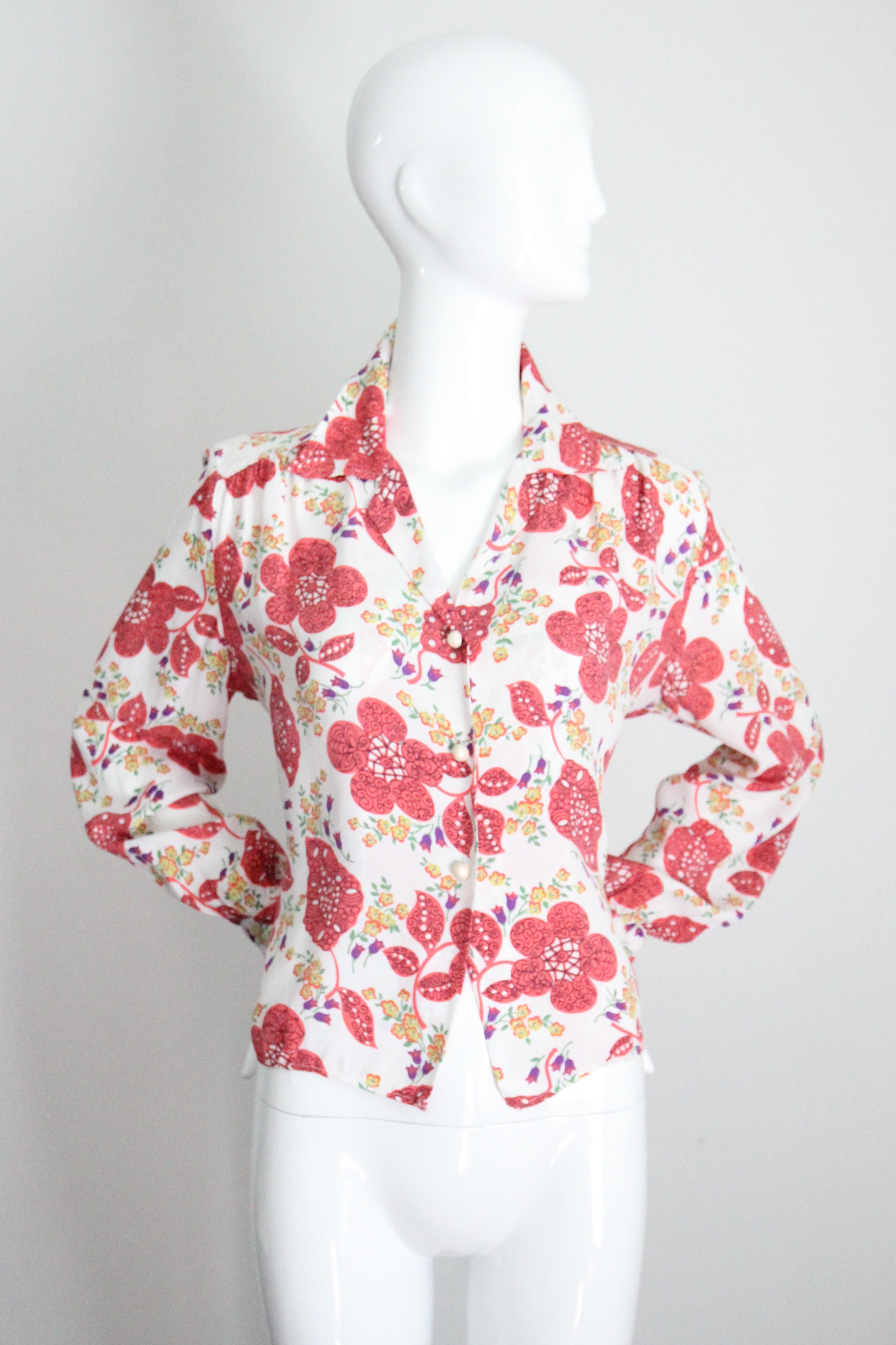 Diese leuchtende Blumenbluse aus den 1940er Jahren in einer Farbpalette aus Korallenrosa, Chartreusegrün, Orgel und Violett mit schwarzen, linearen Akzenten auf weißem Hintergrund,  ist das perfekte Teil für Ihre Alltagsgarderobe.

Der V-förmige