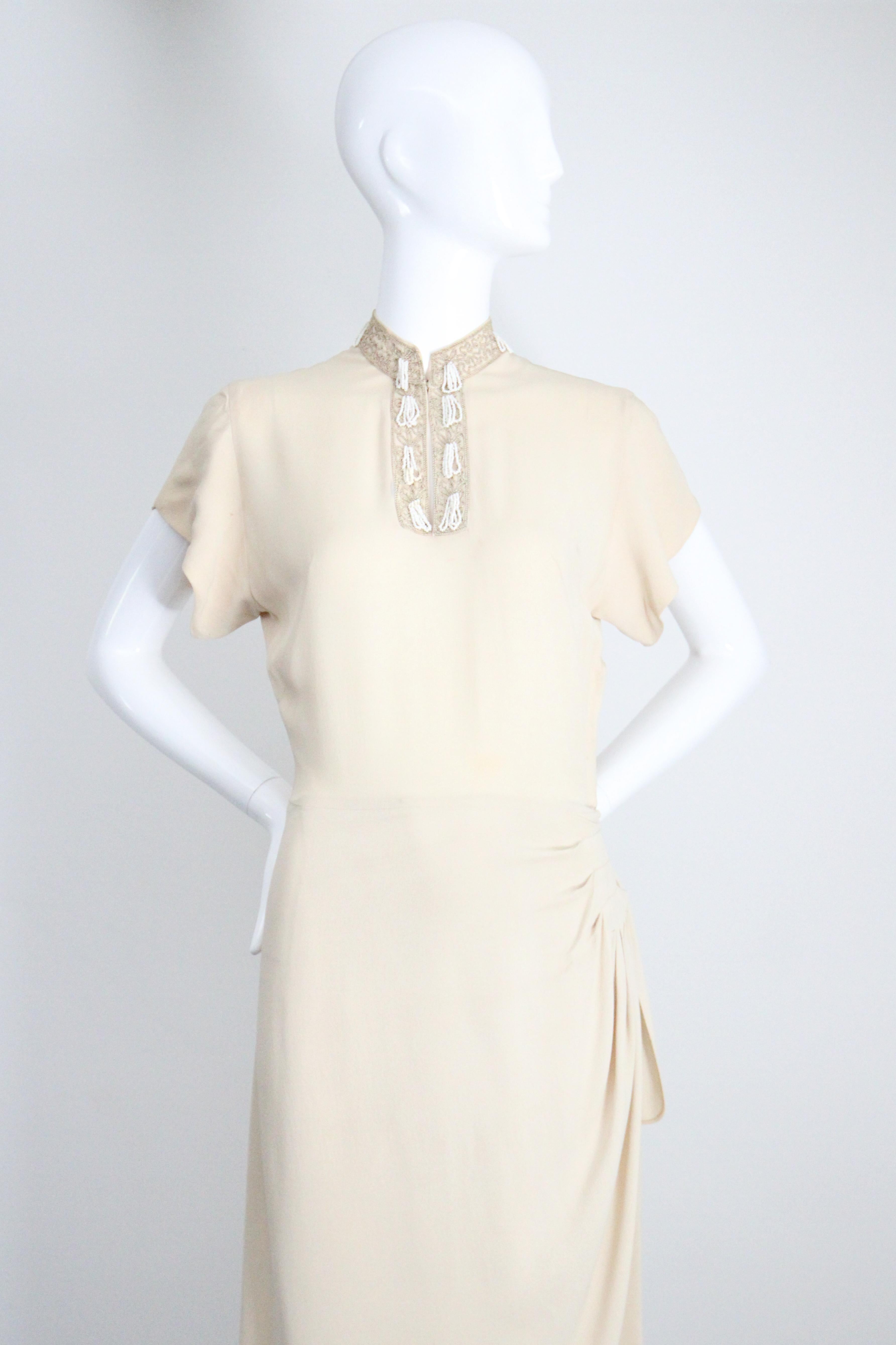 This elegant 1940's cream crepe silk dress, accented by cream and black embroidered soutache which is in turn embellished with white rocailles beaded tassels,  is the perfect piece for your vintage collection. 

The Mandarin style collar, draws in