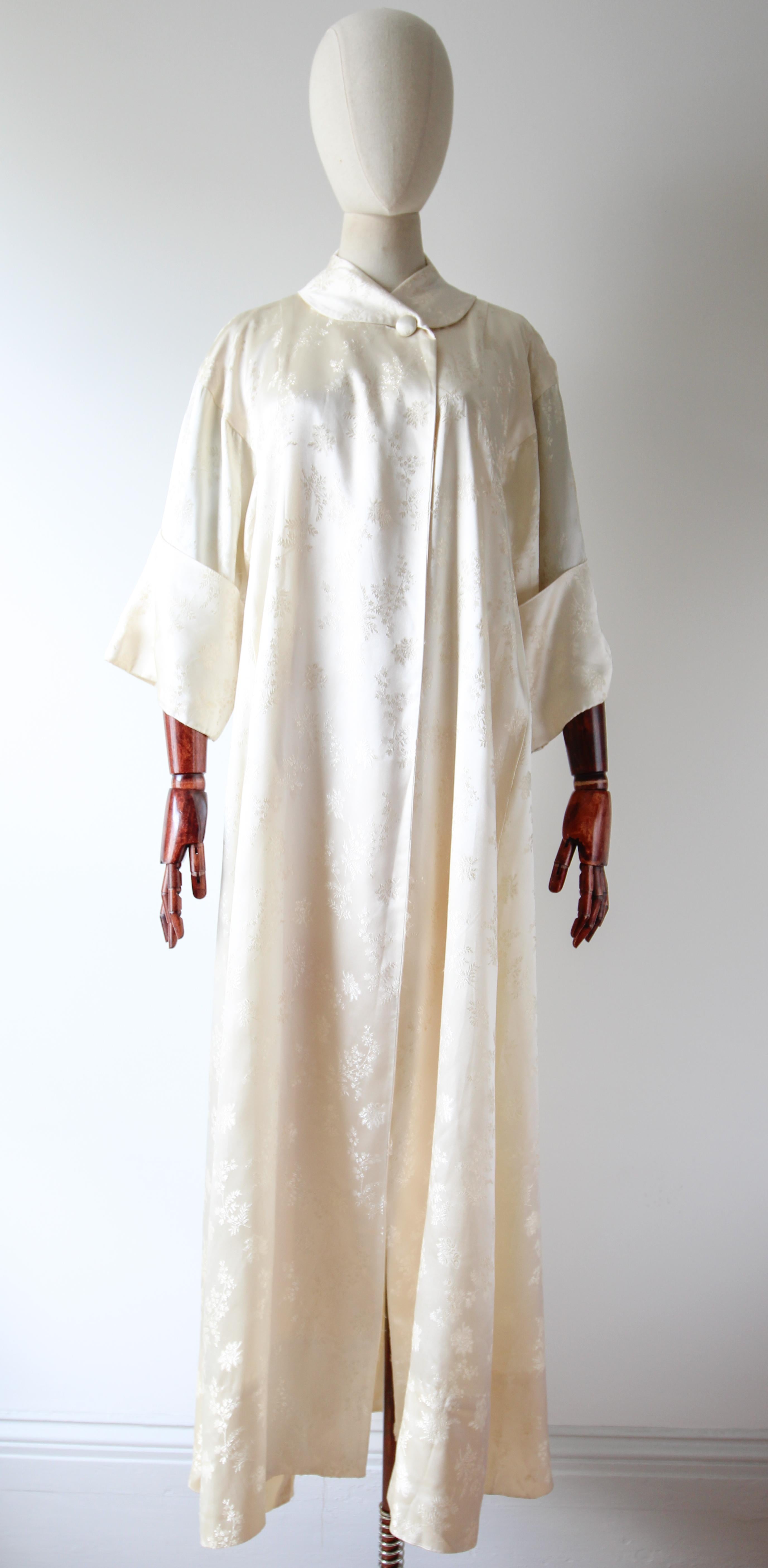 This truly mesmerising 1940's evening coat, rendered in a cream satin brocade with a delicate trailing floral pattern, is the perfect addition to your evening wardrobe. 

The V shaped neckline is framed by a soft shawl collar, which crosses over