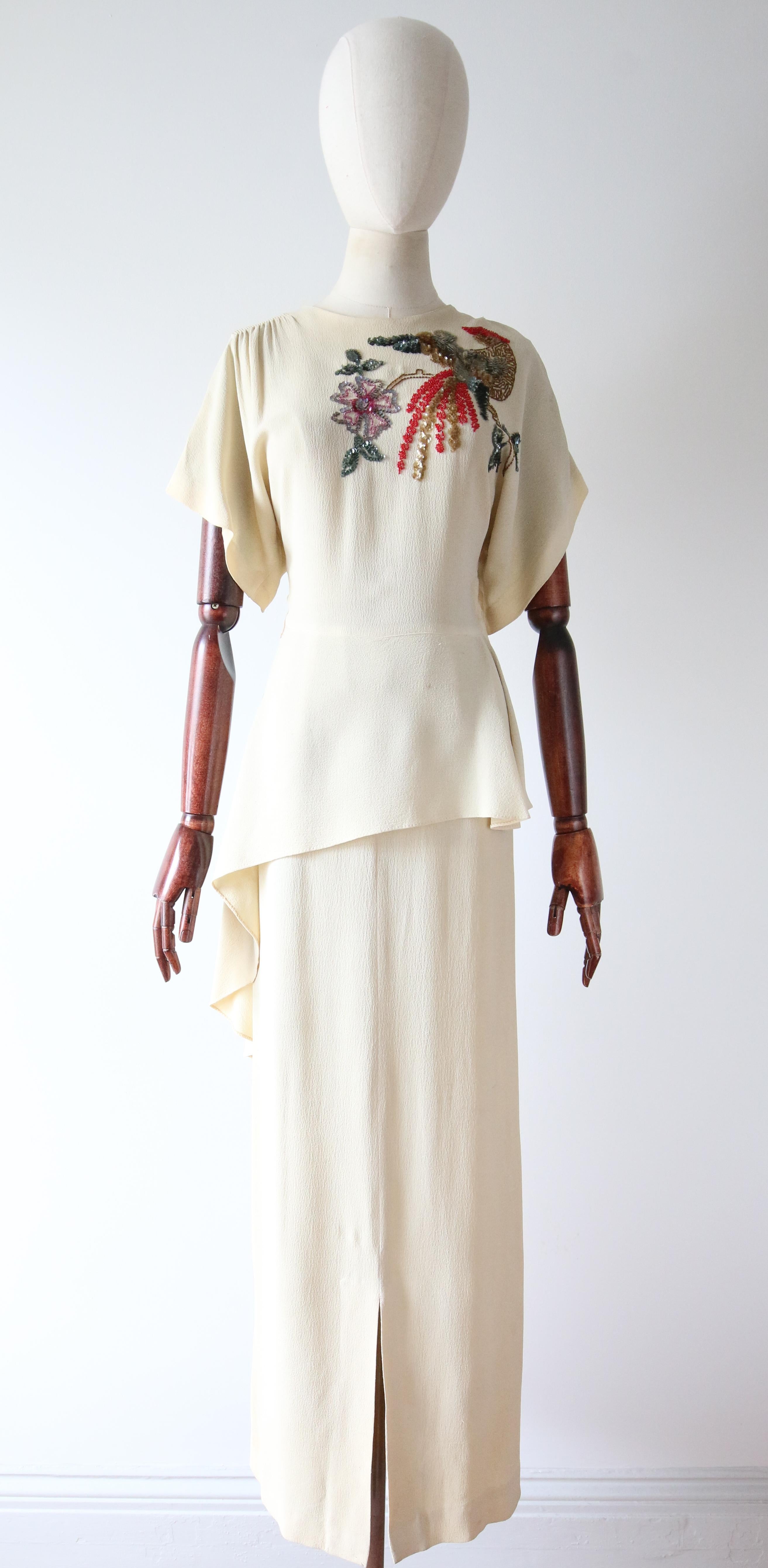 This truly enchanting 1940's cream crepe silk dress, embellished with a sequin and bead design of a bird of Paradise perched upon a branch surrounded by leaves and flowers, in sumptuous shades of gold, red, green and lilacs, is the perfect show