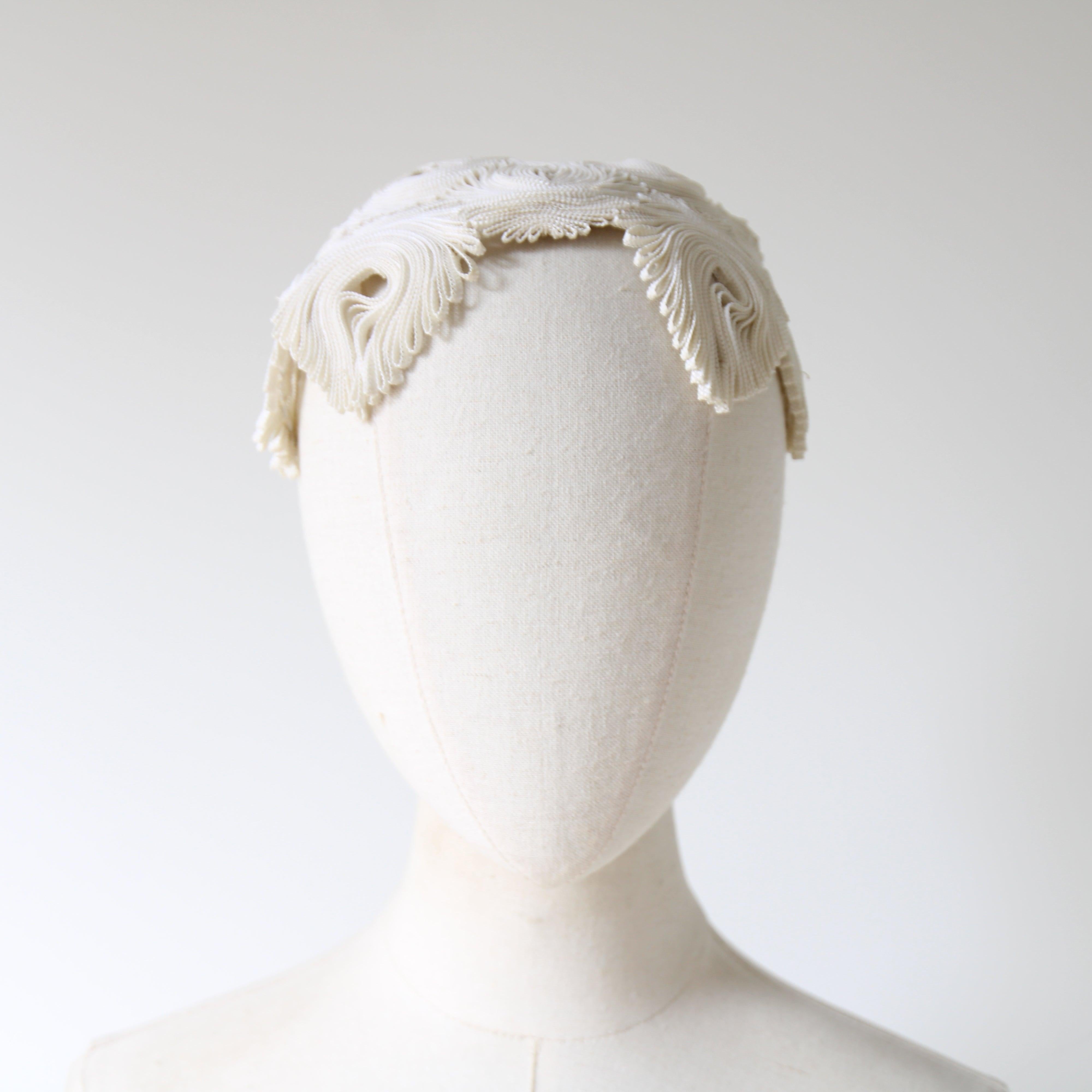 This truly intricate 1940's hat, rendered in a cream plastic braid, which has been folded and pleated in an intricate coral like design, is a rare piece to behold. The rounded crown of the hat, showcases pointed and scalloped edges, built on a wire