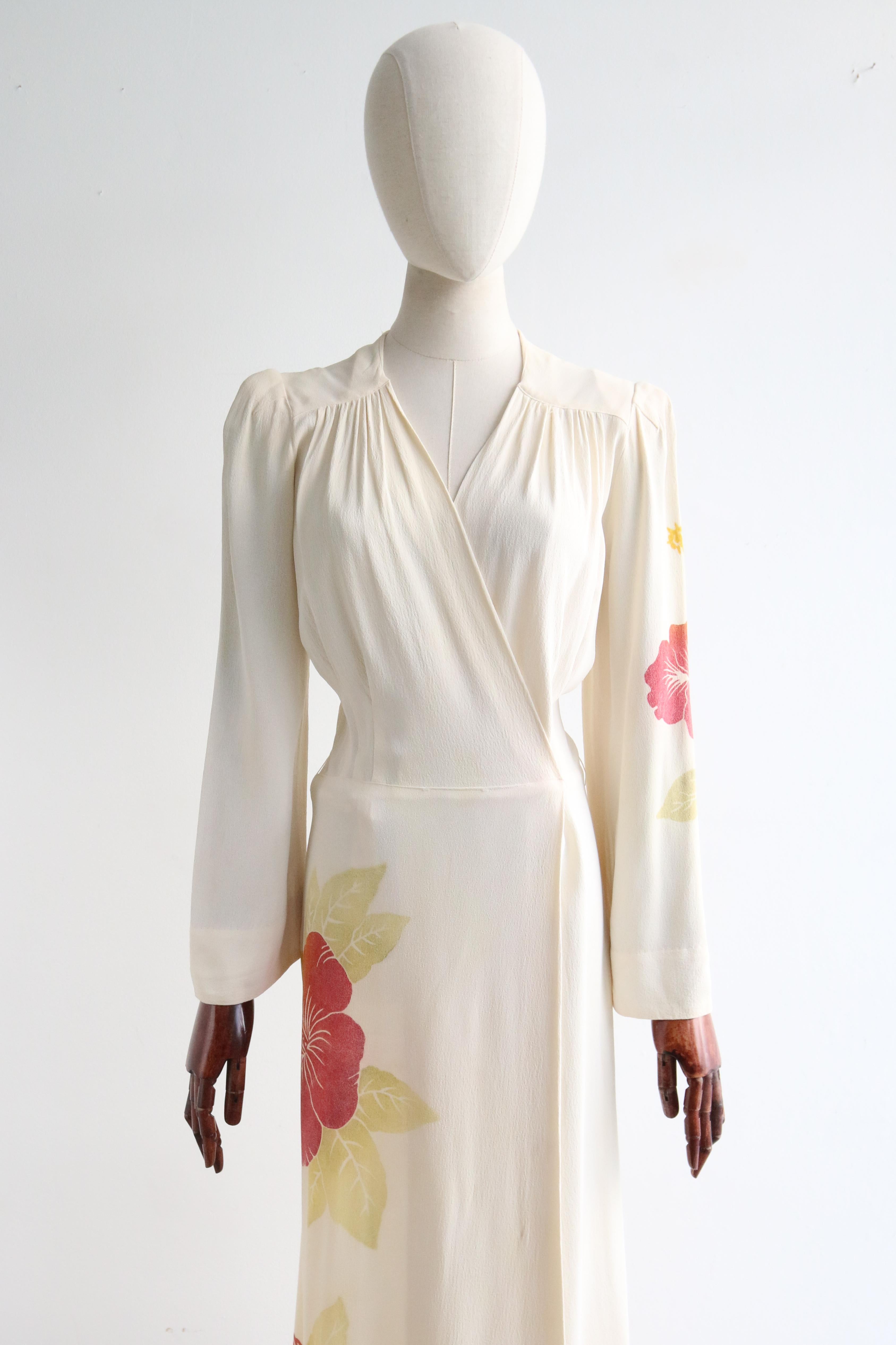 A beauty to behold. This original 1940's dress, rendered in a cream crepe silk, with a pattern of blooming hibiscus flowers in sunsets shades of reds, oranges and yellows, with green leaf accents, is just the piece for that special occasion. 

The