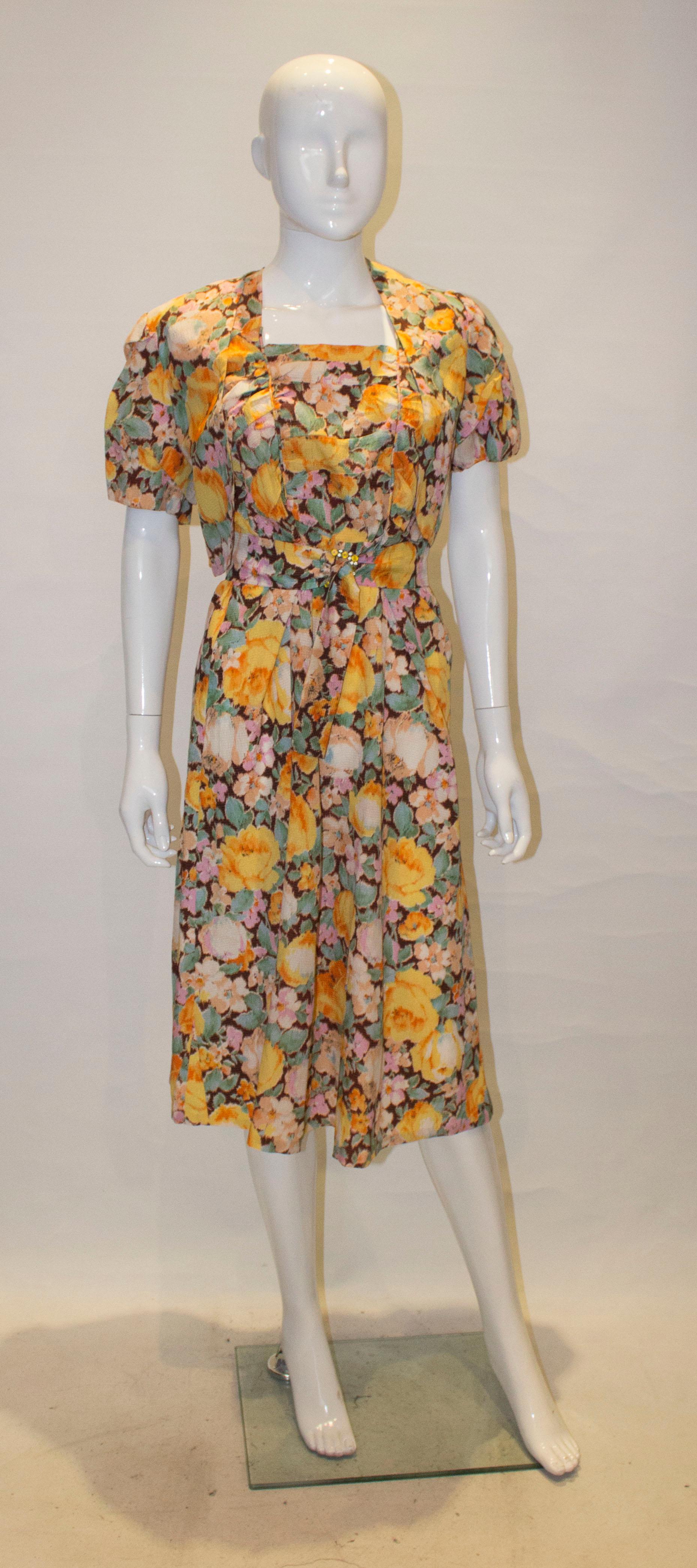A pretty vintage dress from the 1940s. In a floral print of brown , yellow, green and beige, the dress has a square neckline with pleat detail at the front. There is a matching bolero, and self fabric belt.

Measurements: Dress bust 35'',length