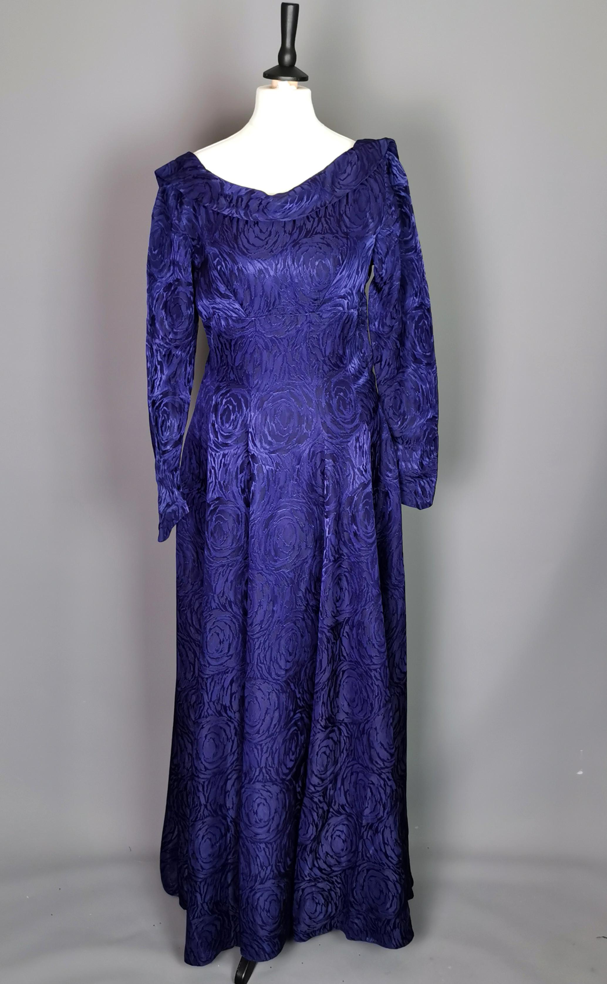 A simply stunning vintage late 1940s evening dress.

Made from a very heavy, purple satin Brocade fabric with a swirling floral pattern.

It has long tulip sleeves that fasten at the wrist with press stud fasteners, the neckline is scooped with a