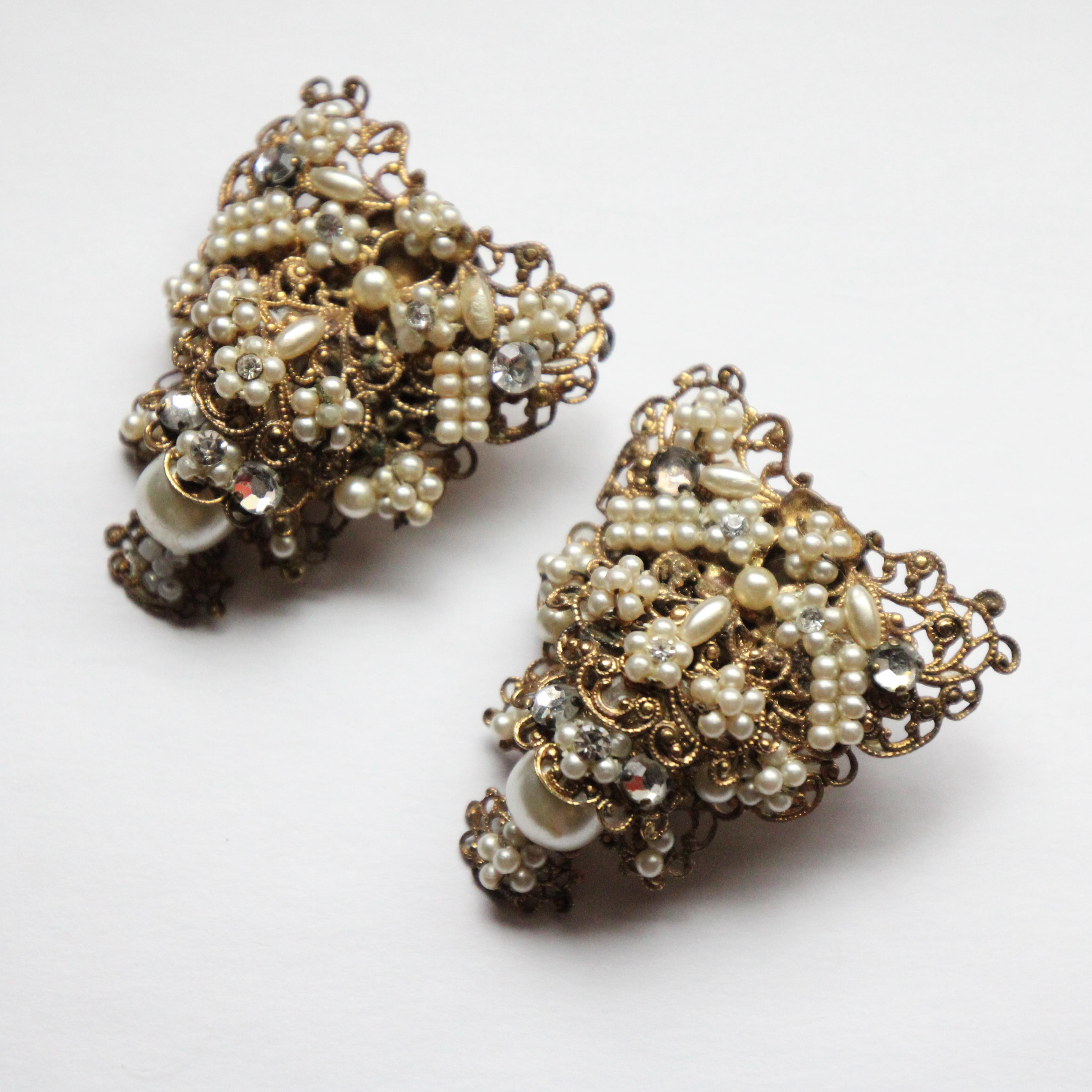 These spectacular 1940's screw back earrings, accented by small pearlescent beads, silver claw set rhinestones and inlaid rhinestone,  are the perfect statement piece to your outfit.

Constructed on a gold toned metal filigree base in a triangular
