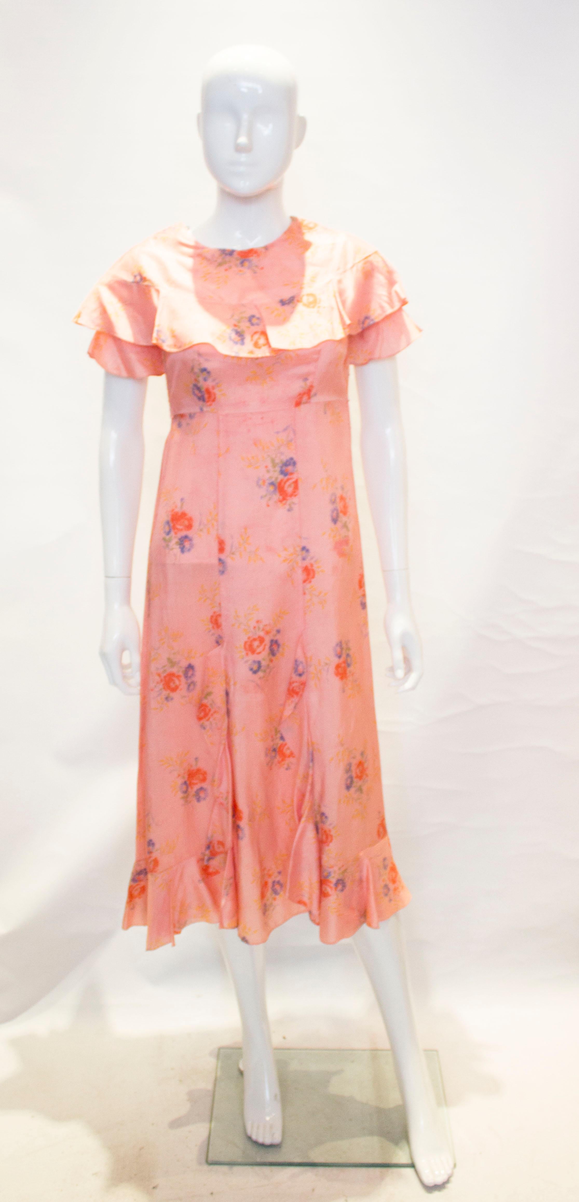 A pretty vintage pink floral dress. It has a popper opening at the shoulder and side..It has ruffle detail on the neckline and lower front and hem.