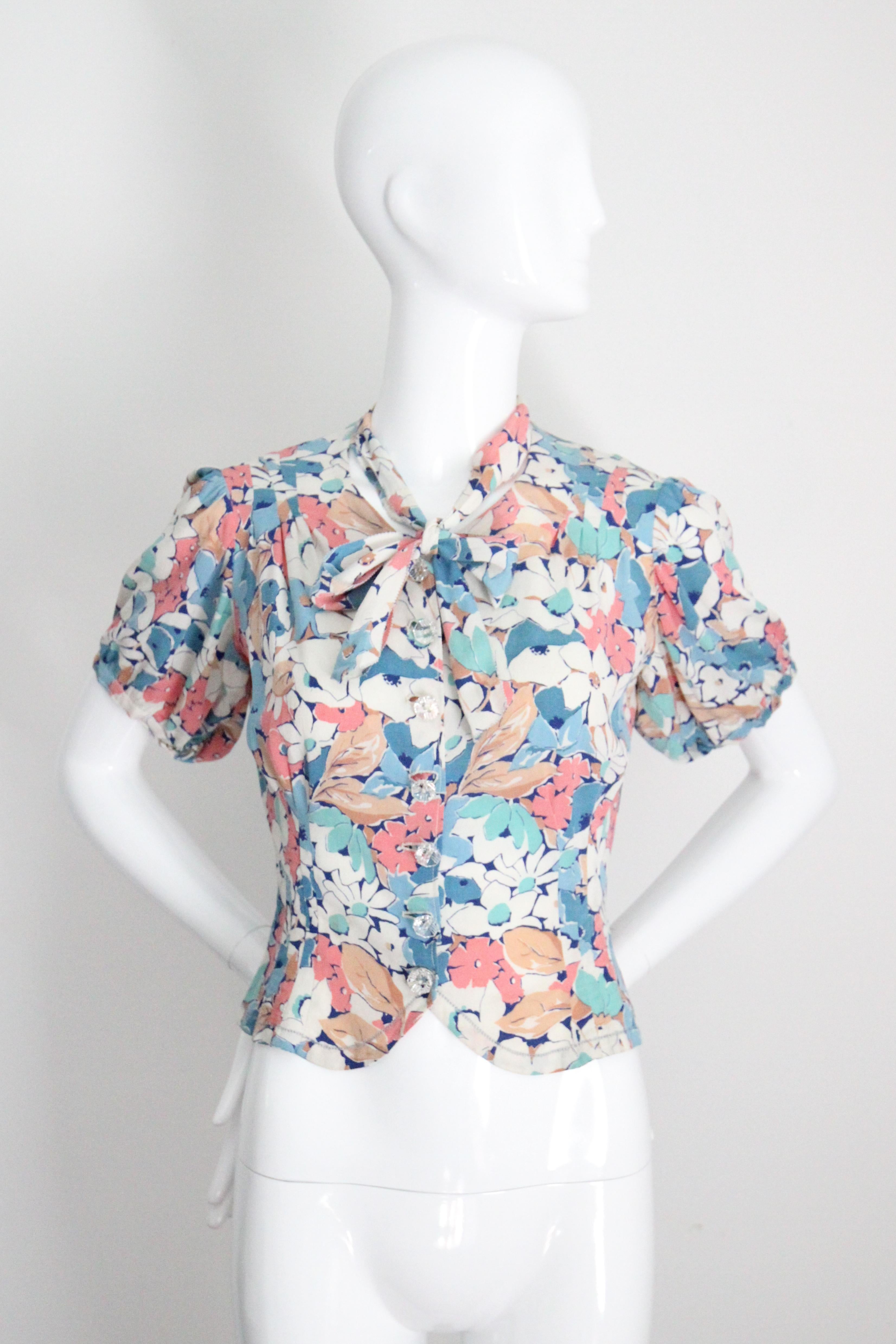 This wonderful 1940's crepe silk blouse, in a floral print in a palette of pinks, blues, sea greens and tans, with navy blue and cream accents, is the perfect piece for adding to your everyday wardrobe. 

The soft  V shaped neckline is accented by a