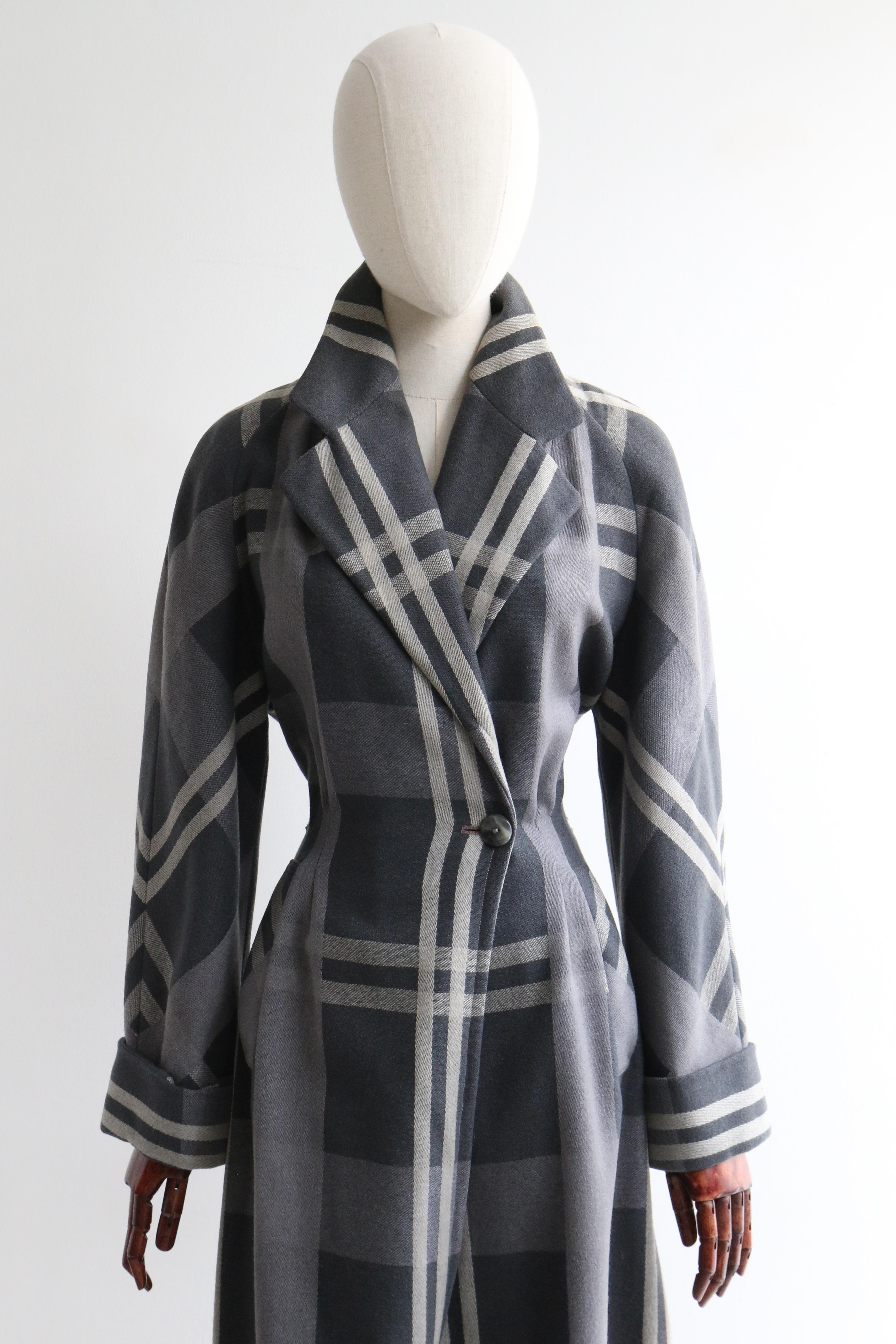 This truly magnificent 1940's wool coat in a wide plaid woven pattern, in shades of grey, fully lined in silk, is the perfect addition to your seasonal wardrobe.

The V shaped neckline is framed by a notched collar that joins the front of the coat