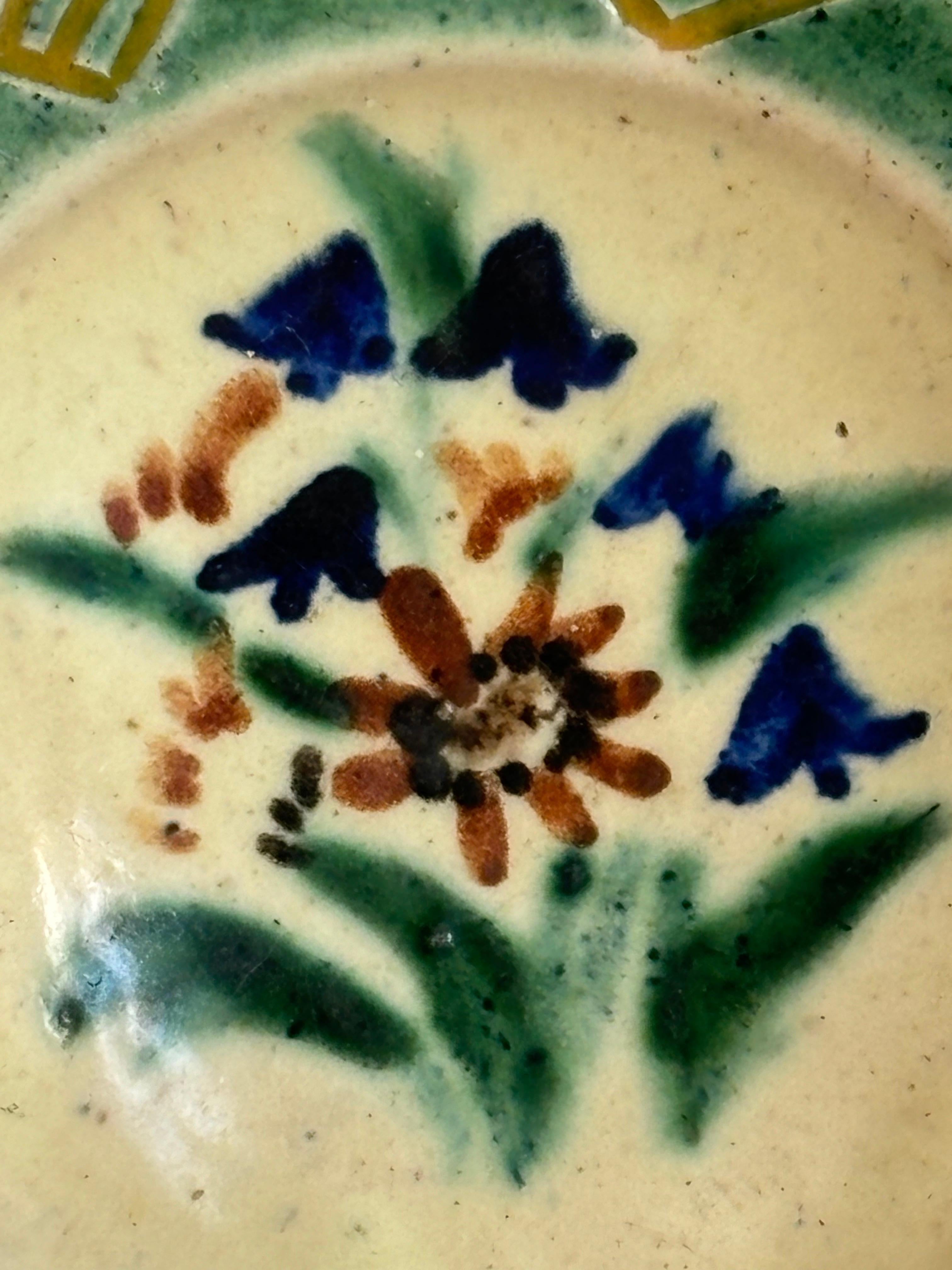 Piccola ciotola decorativa vide-poche in ceramica con decorazioni floreali dipinte a mano nei colori dell'ambra bruciata, del verde e del blu. Grafica in rilievo lungo i bordi smaltata con sfumature ocra e verdi. Timbro sotto la base. Buone