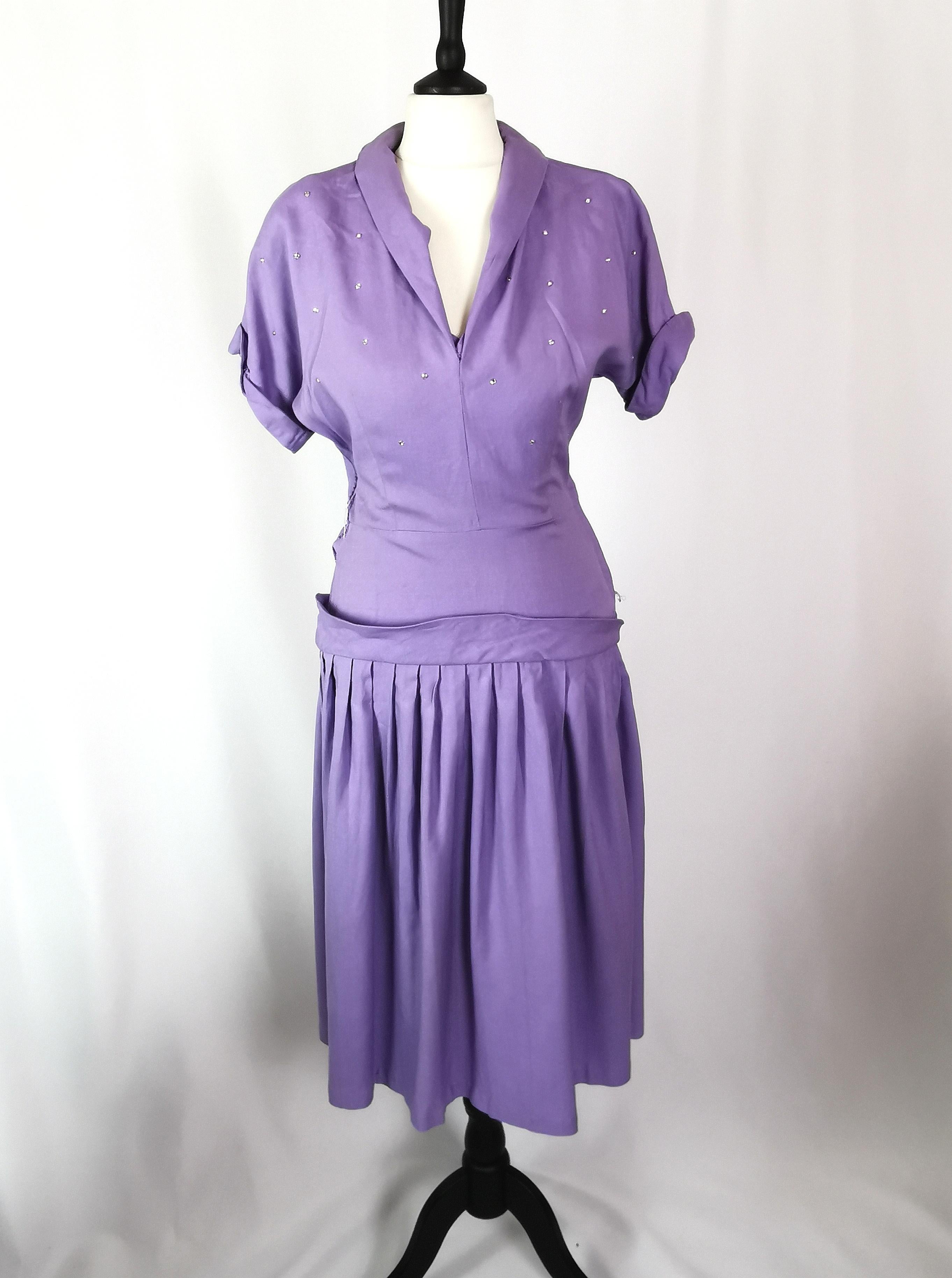 Une robe lilas vintage des années 1940 tout simplement stupéfiante.

Fabriqué à partir d'un mélange de coton lourd et de laine dans une couleur lilas vibrante, il est à hauteur du genou avec une jupe complète.

La robe a des manches courtes avec un