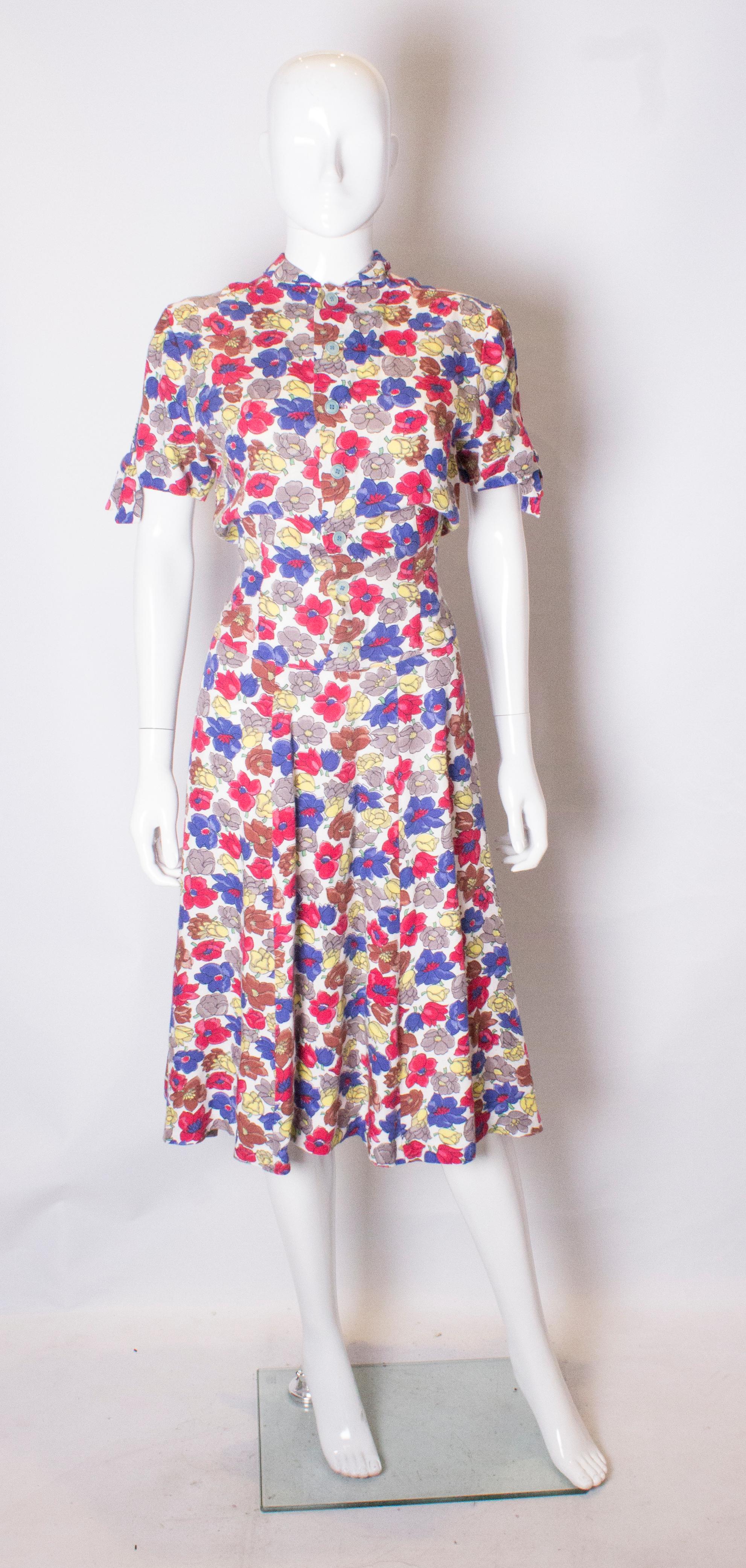 A pretty vintage day dress from the 1940s. The dress has a white background, with crimson, blue , brown and yellow flowers. It has a decorative bow on either sleave and a self fabric tie belt so he dress can be belted to your size. It has a seven