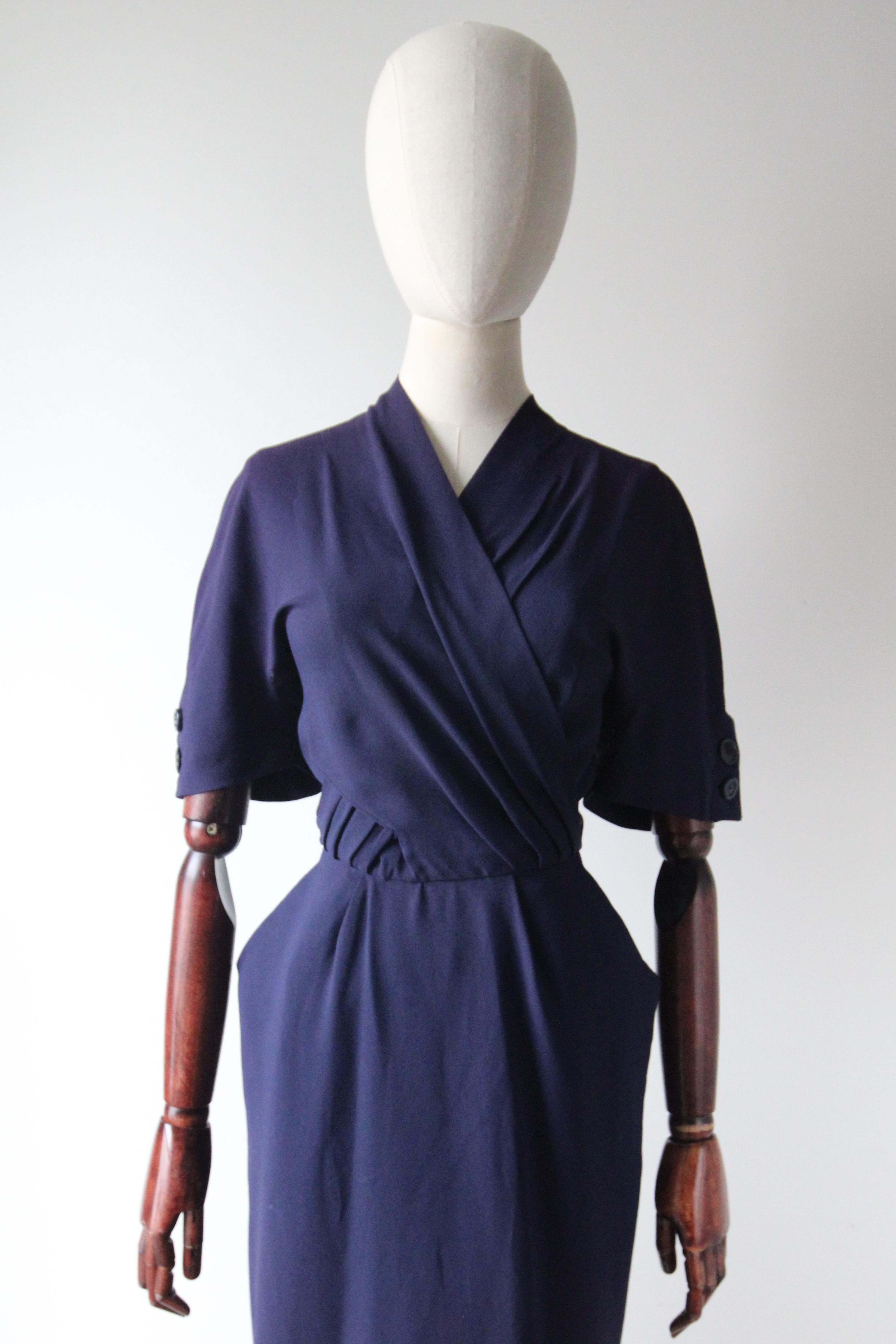 Rendered in the most delightful shade of navy blue crepe silk, this original 1940's dress, accented by a cross over feature and button fastenings along the length of the back of the dress, is just the piece for your every day wardrobe.  
The V