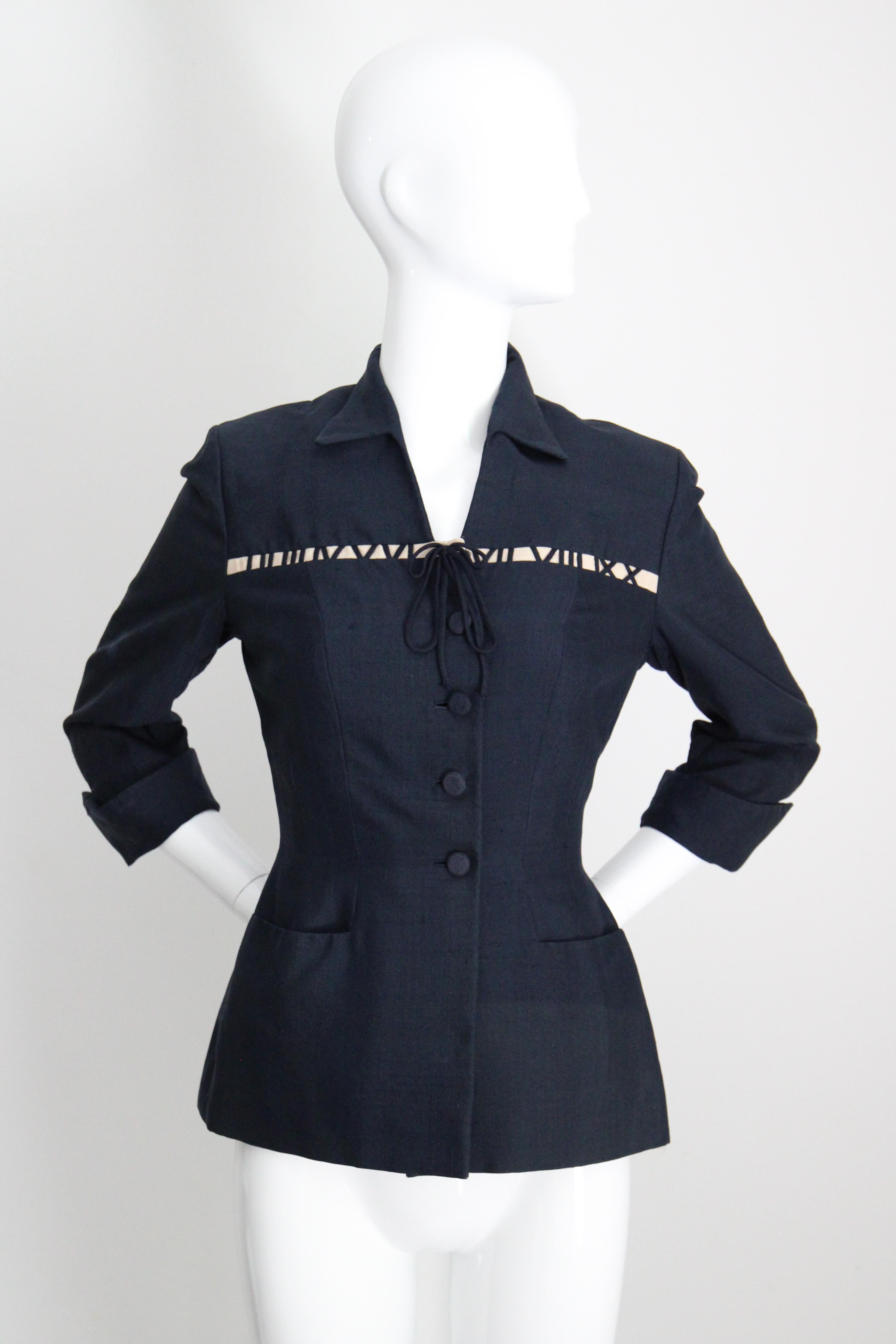 Esta chaqueta de seda azul marino Gene Shelly de la década de 1940, bellamente confeccionada y con números romanos, es la prenda perfecta para tu armario vintage. 

El escote en V está enmarcado por un fino cuello en punta, que realza la elegante