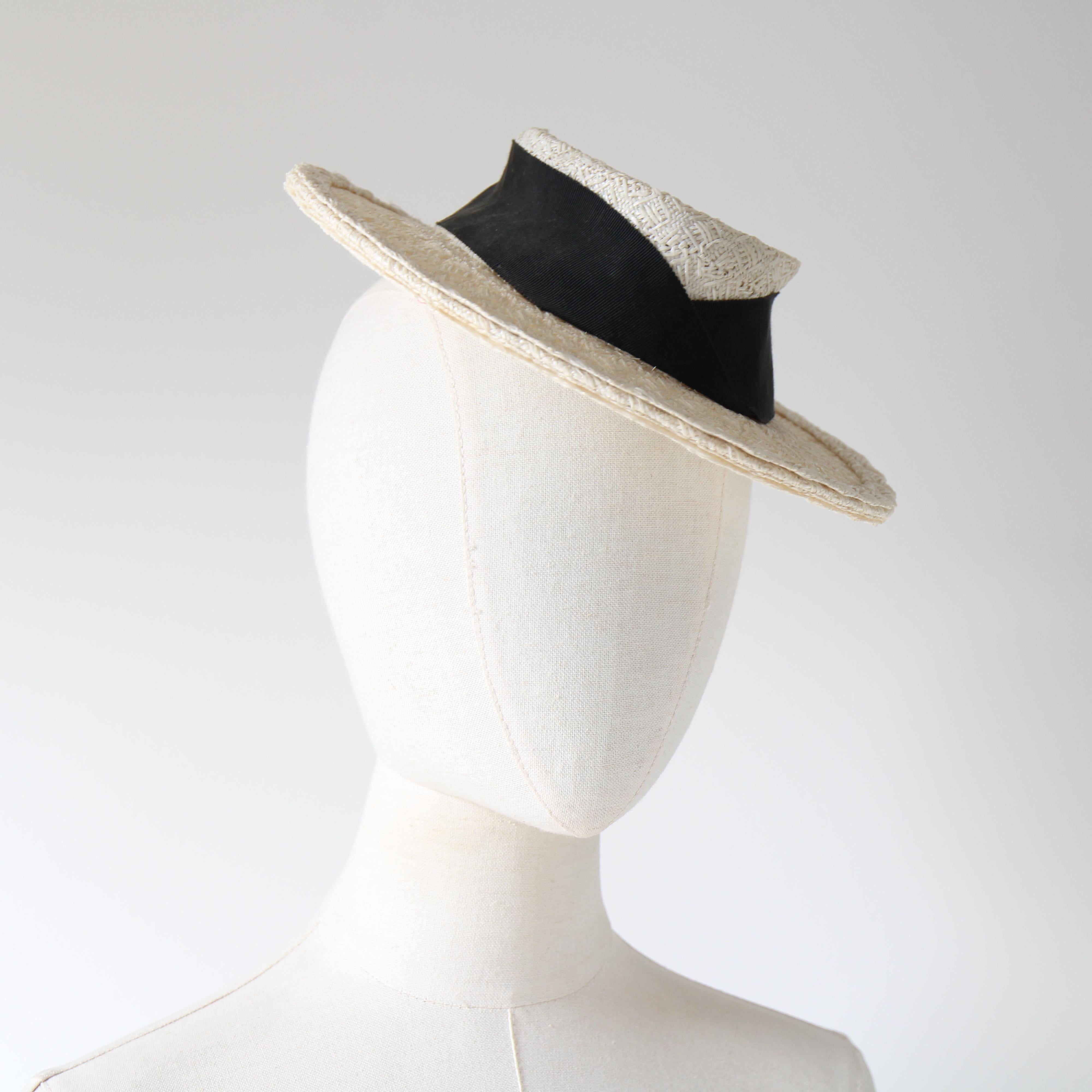 This statement 1940's straw percher hat, in a monochrome palette, with a white straw base set against a black faille ribbon is a rare piece to behold. 

The wonderful slim brim, frames the miniature crown, which boasts a slightly curved top. The