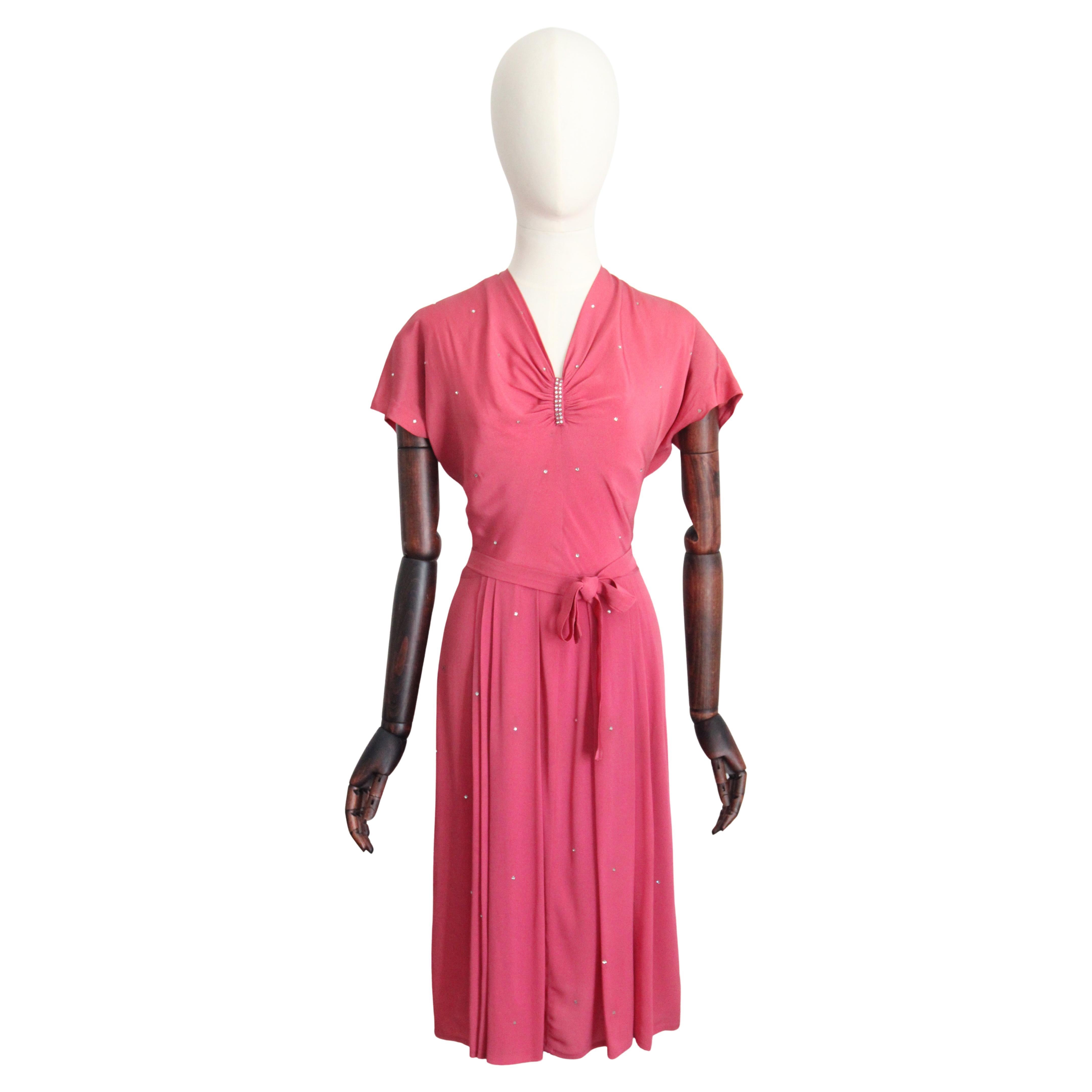 A beauty in blush. This original 1940's pink silk dress, embellished with scattered claw set silver rhinestones, is the perfect piece to add to your vintage collection.  

The V shaped neckline of the dress, is accented by gathered and drawn in