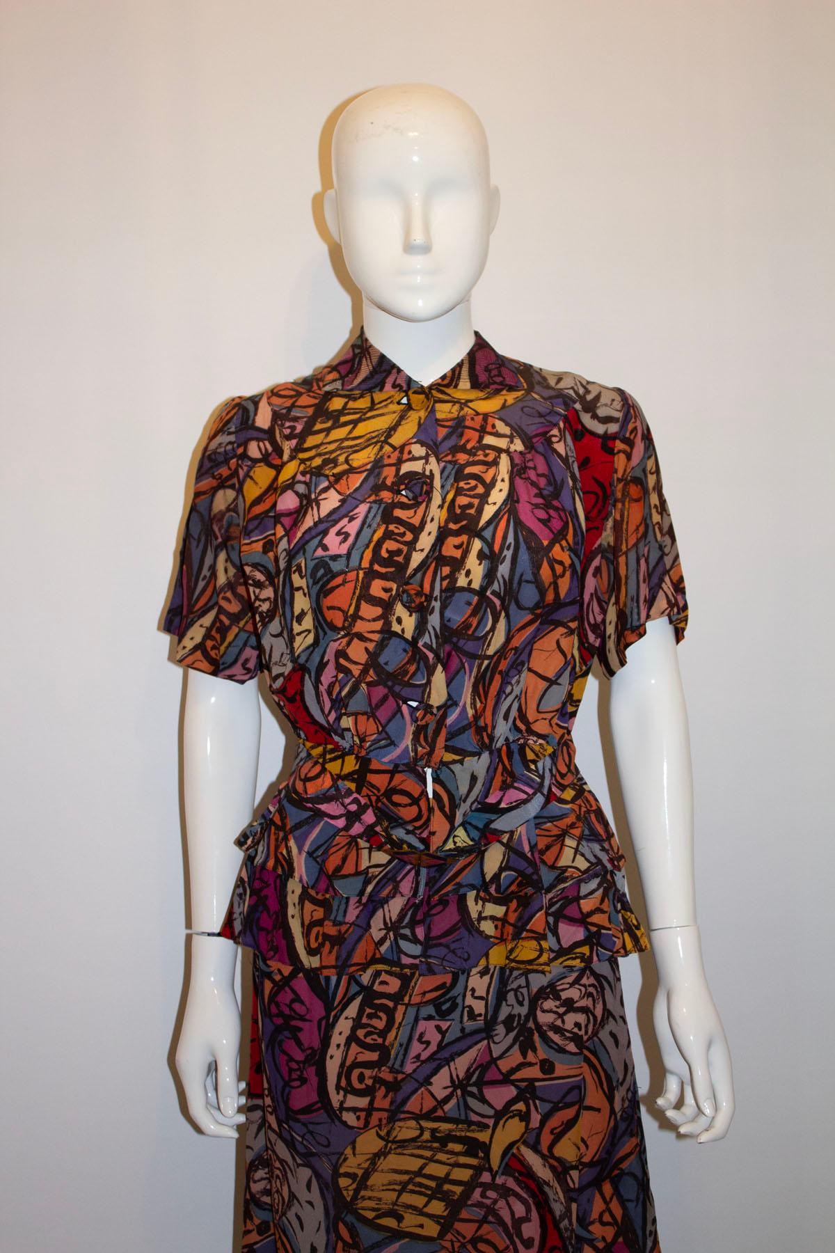 Un tailleur jupe vintage des années 1940 qui fait tourner les têtes. Le costume est composé d'une magnifique impression de violet, de rose et d'orange. La jupe est en ligne A, et la veste a une ouverture à boutons en tissu, un empiècement et un