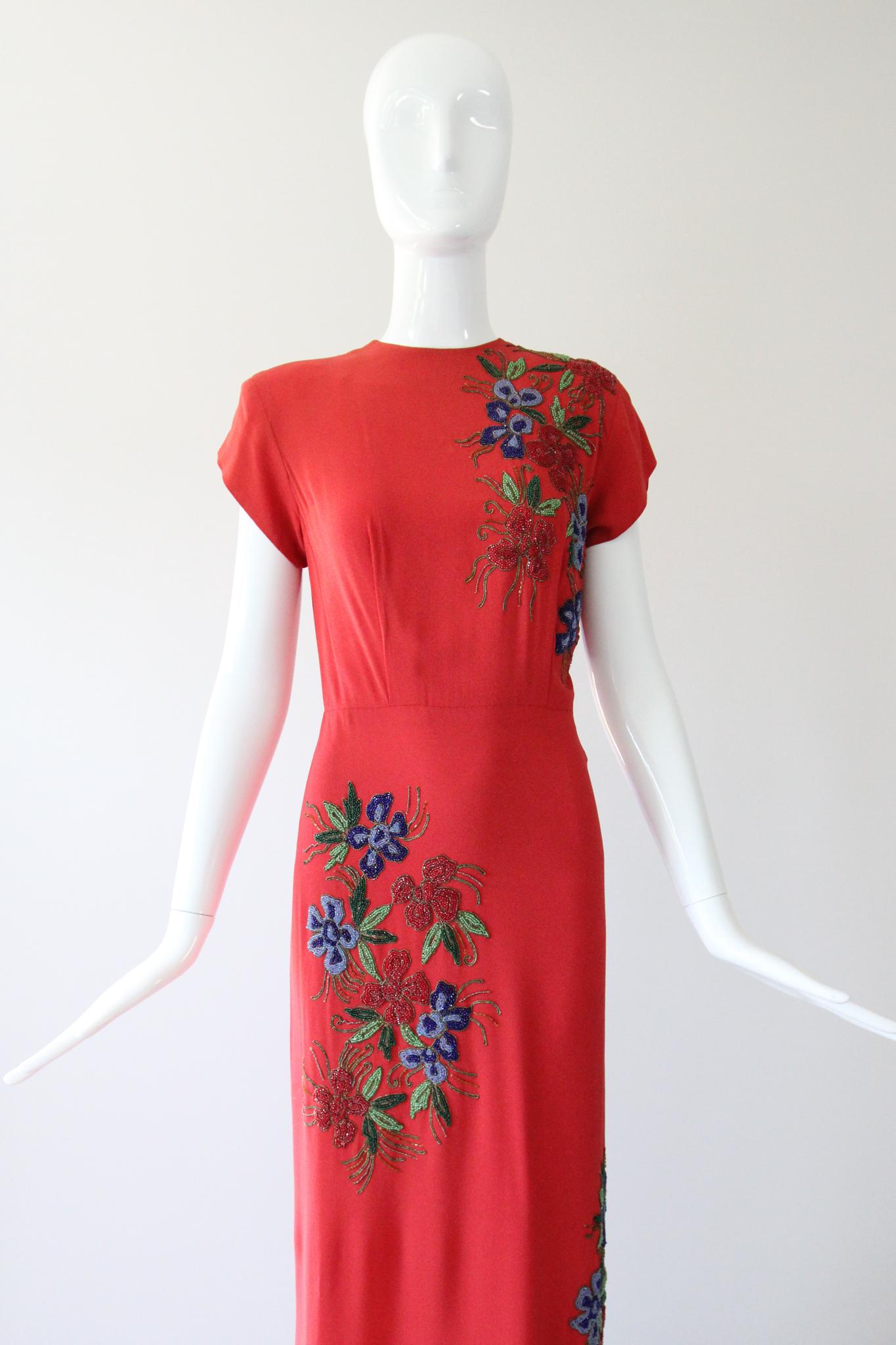 Cette robe en crêpe de soie des années 1940, d'un rouge vermillon des plus éclatants, ornée de broderies en soutache lamé or entourant des perles florales dans des tons bleus, rouges et verts, est le fleuron parfait de votre collection vintage.