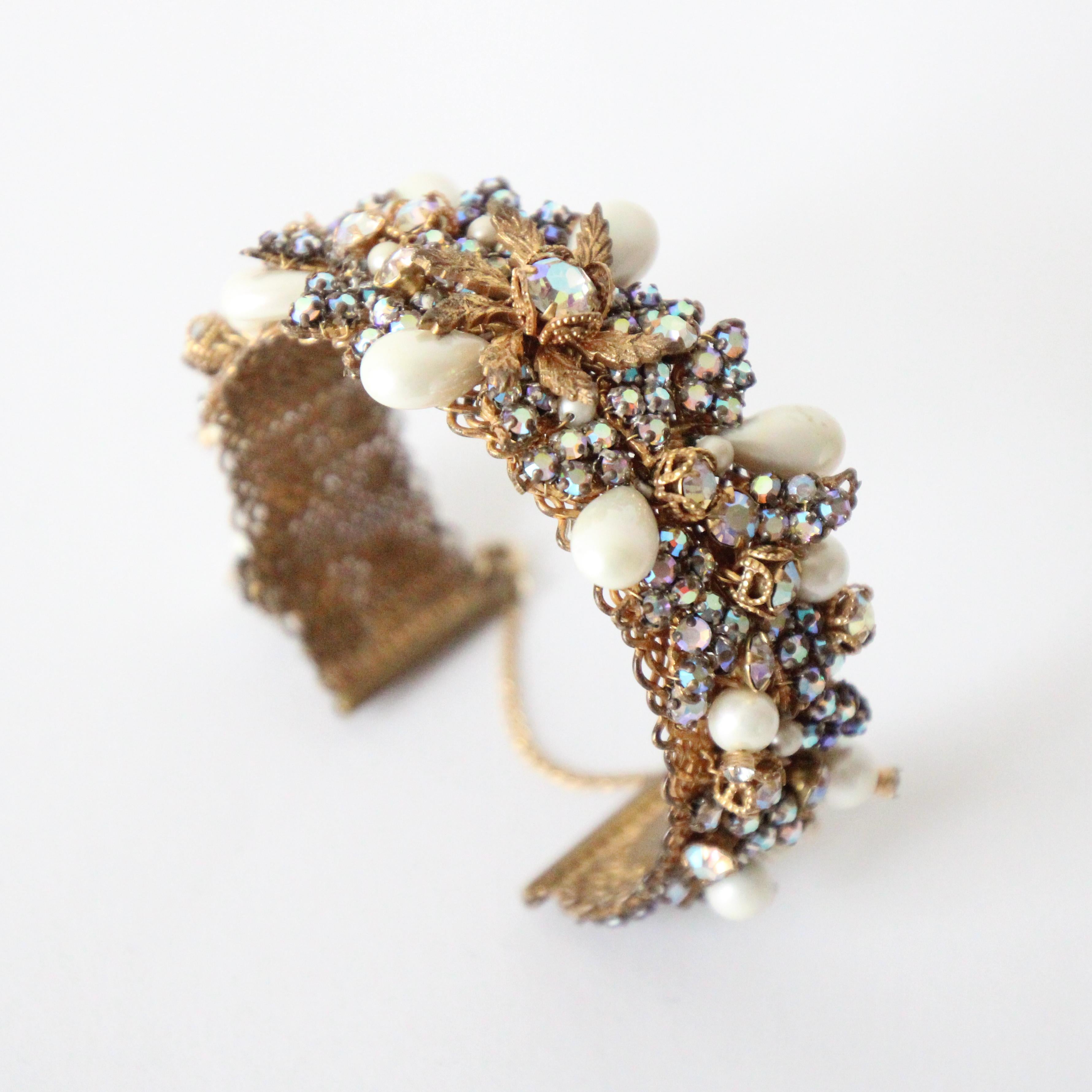 Cet époustouflant ensemble de demi-parures en strass irisé et perles de Robert DeMario des années 1940, composé d'une paire de boucles d'oreilles et d'un bracelet assorti, est très rare.

L'élégant bracelet bangle est doté d'une base en métal en