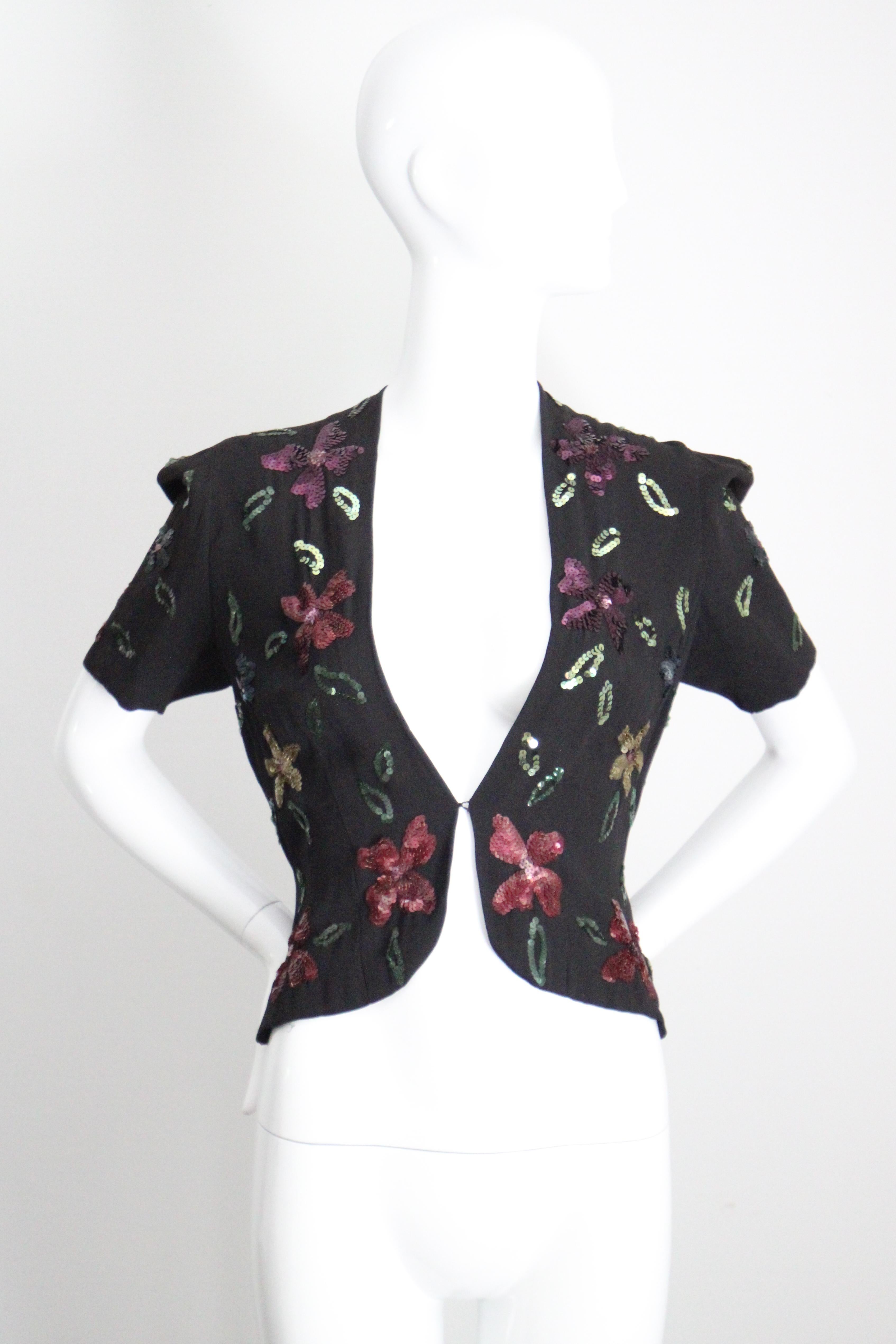 This truly captivating 1940's black rayon jacket, embellished with a pattern of sequin scattered flowers and leaves in shades of purple, green, gold, pink and blue, is just the perfect statement piece to add to your vintage collection.

The V shaped