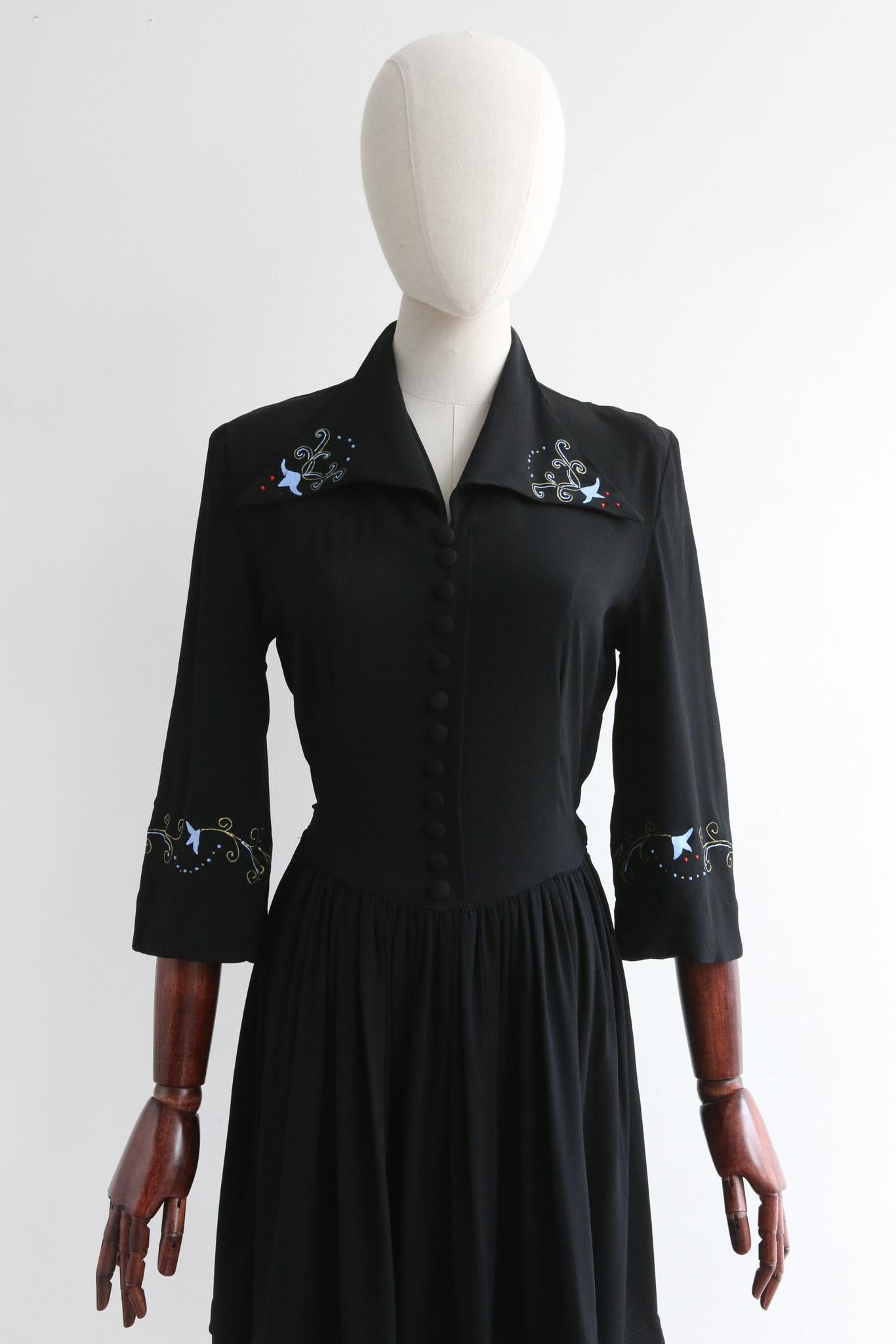 This truly breathtaking 1940's black crepe silk CC41 dress, with a hand painted and printed trailing pattern of blue bells and filigree decorative gold stems, is a rare piece to behold and never again find. 

Her V shaped neckline is framed by a