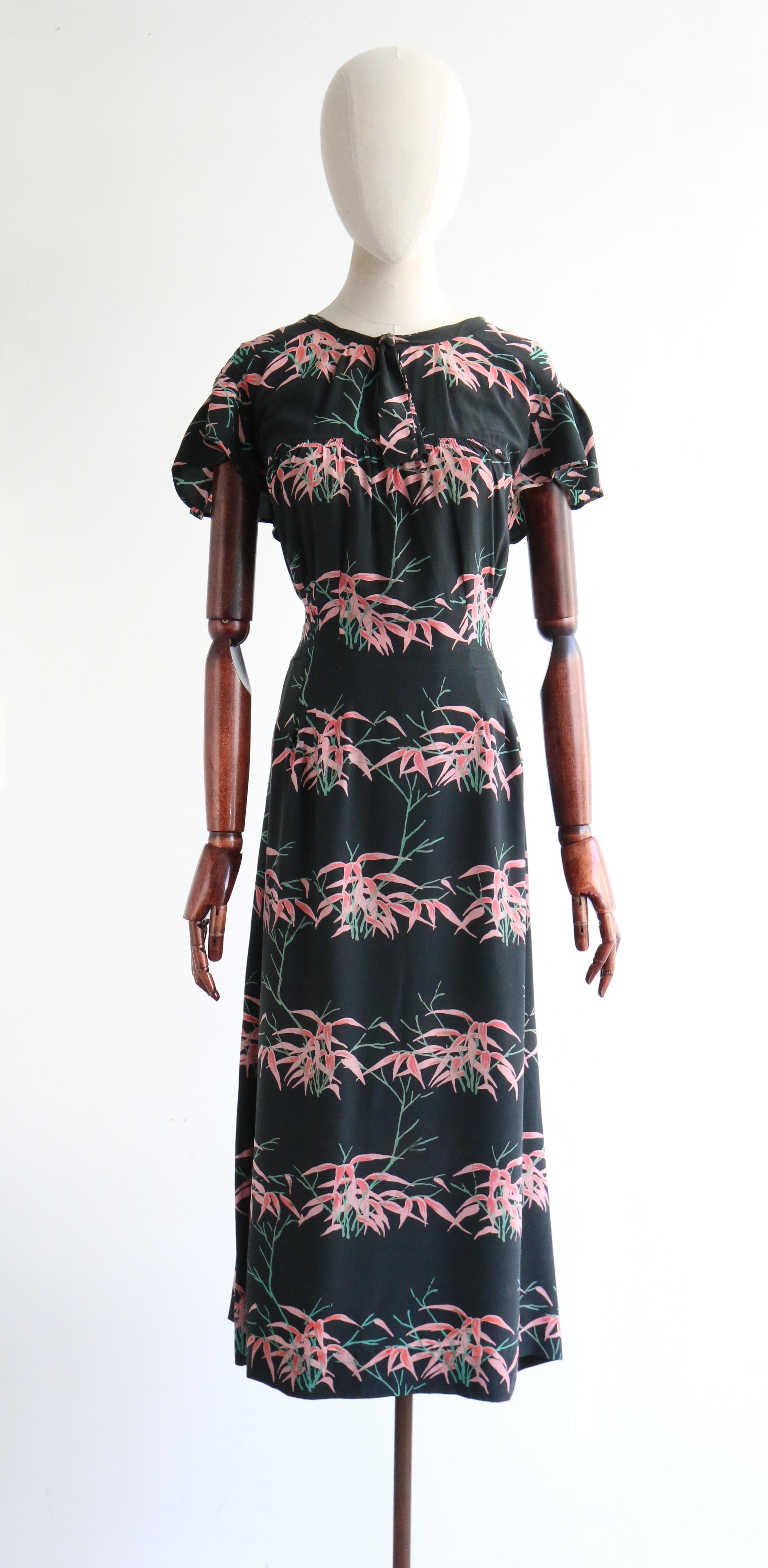 Rendered in an abstract floral design in shades of pink and green, set against a black silk base and in a striped pattern, this original 1940's dress and matching jacket is the perfect addition to your seasonal wardrobe. 

The rounded neckline of