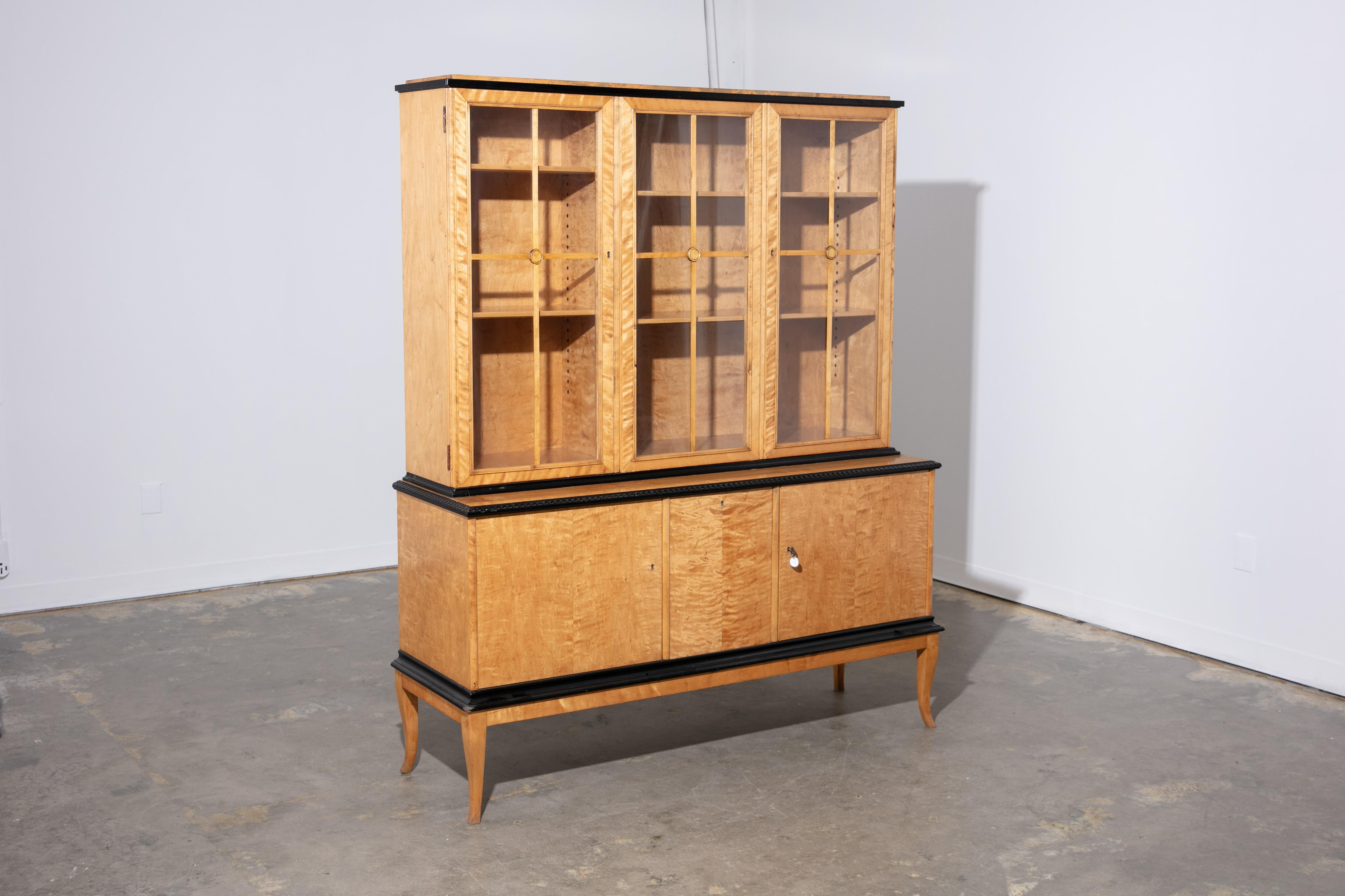 Vintage 1940's Swedish Biedermeier style china cabinet with locking door and adjustable shelves by Fran Blomstermala Mobelfabrik. Black painted edge details. Two piece cabinet rests on four curved, tapered legs giving it an elegant appearance. Light