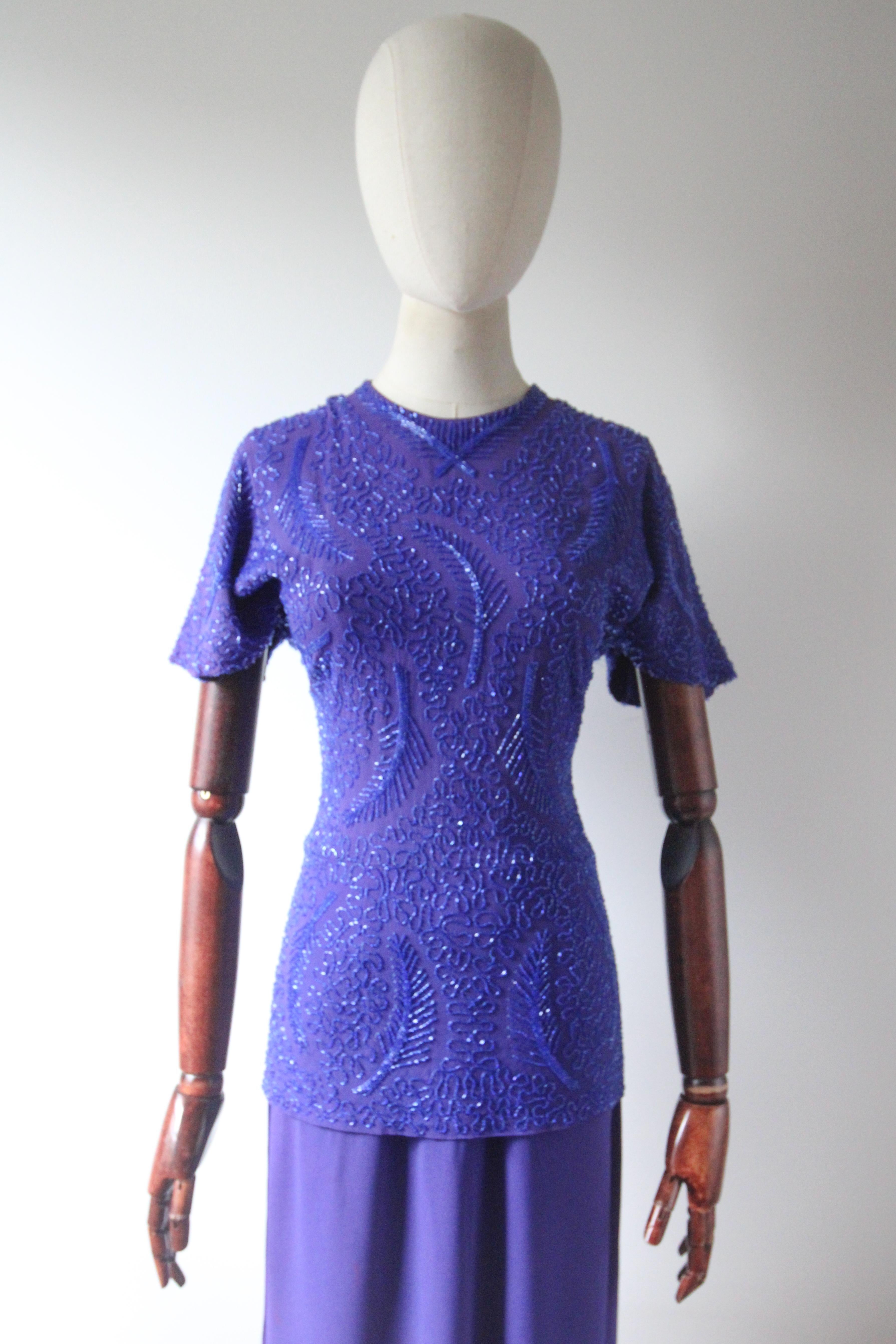 This truly enchanting 1940's violet blue crepe silk dress, embellished with royal blue glass bugle beads, in a trailing swirl pattern with leaf design details, is the perfect show stopper for your vintage collection. 

The rounded neckline of the