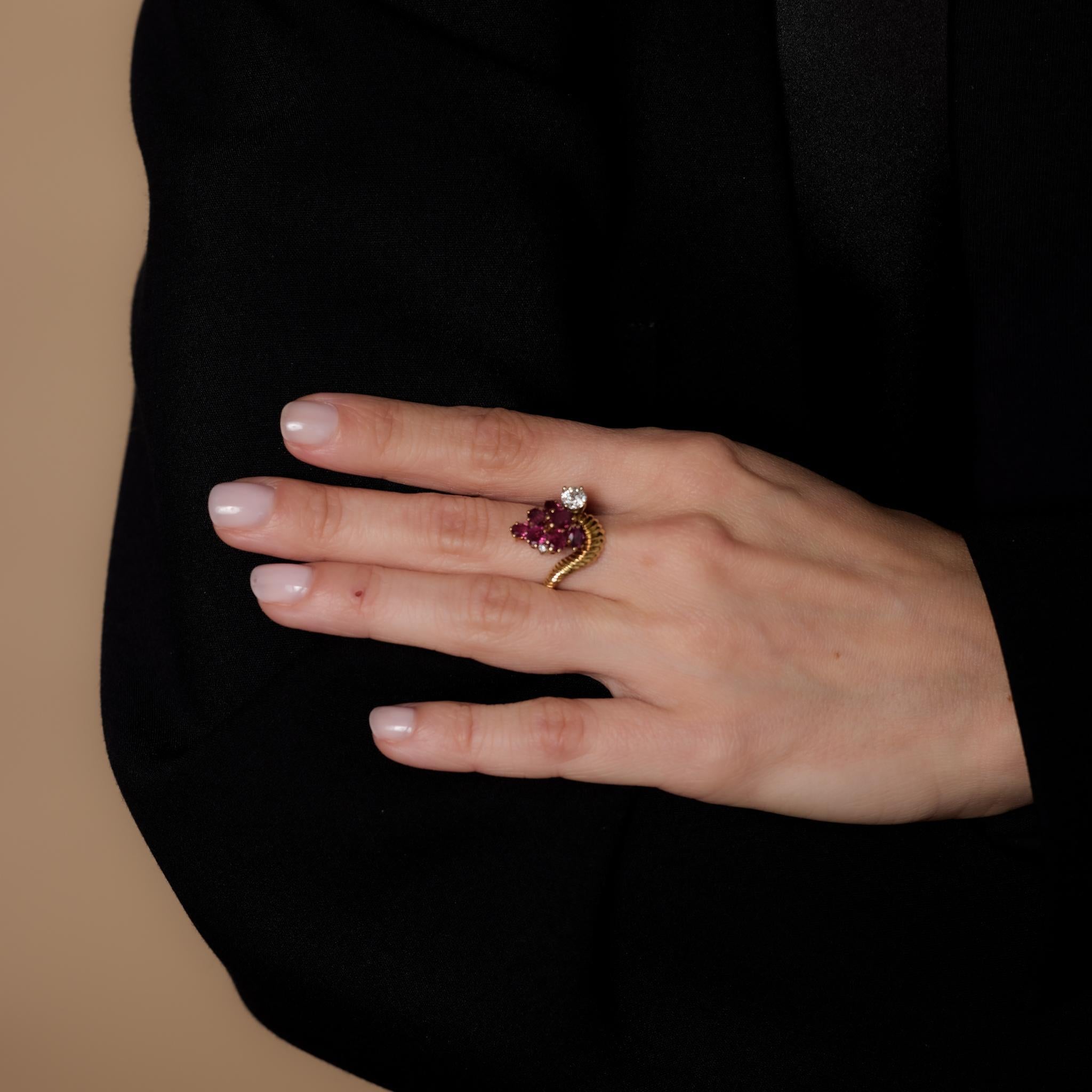 This vintage 14k yellow gold cocktail ring showcases seven oval cut rubies totaling 1.95 carats, accented by two old European and single cut diamonds weighing approximately .50 carats, H-I color, and VS-SI clarity. Crafted in the 1970s, it is