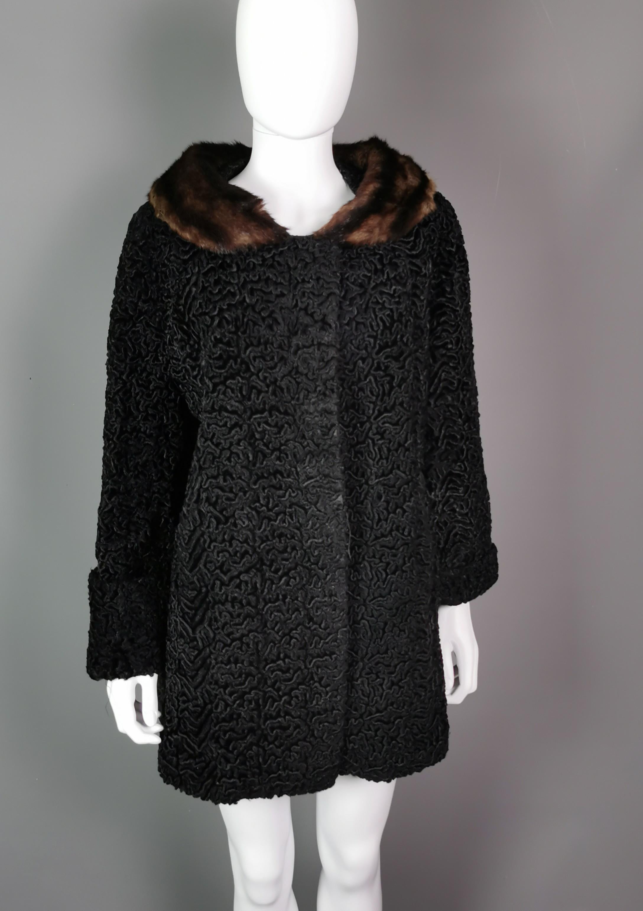 A gorgeous vintage 1950s Astrakhan coat.

Rich inky Black curly lamb wool with a brown mink fur collar.

It is long sleeved, a mid length duster style coat, it has no fasteners, it did have a hook fastener but this is no longer present.

The coat is