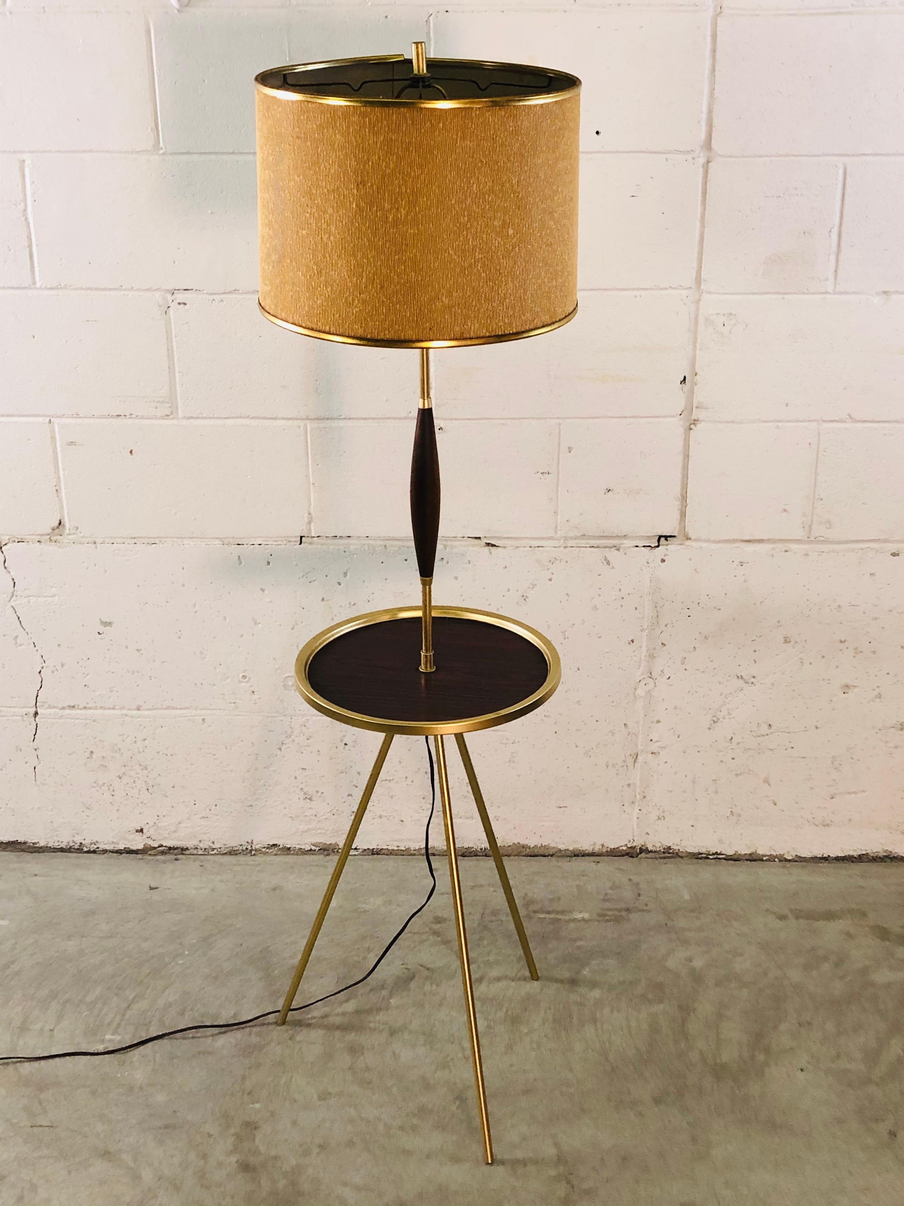 Vintage 1950s atomic style tripod floor lamp with original shade. The lamp has a faux-walnut and brass round tray table. The shade measures: 14.5” diameter x 10” height. The lamp has been newly refinished and is in working condition. No marks.