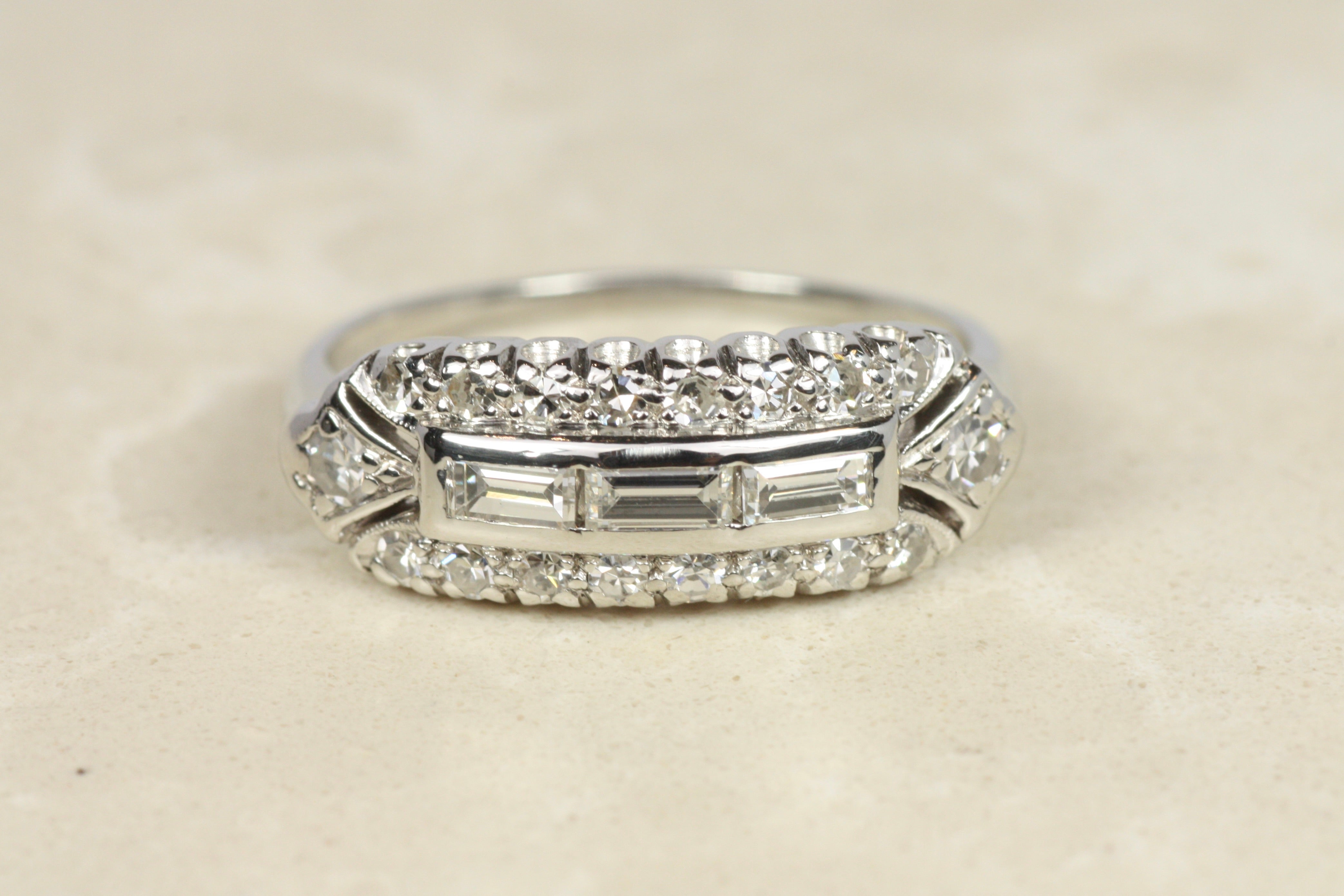 Una preciosa alianza de diamantes vintage de los años 50. La parte superior rectangular de platino está engastada con diamantes baguette en el centro, rodeados de 18 diamantes redondos de talla única en engaste de cola de pez y cuentas. El vástago