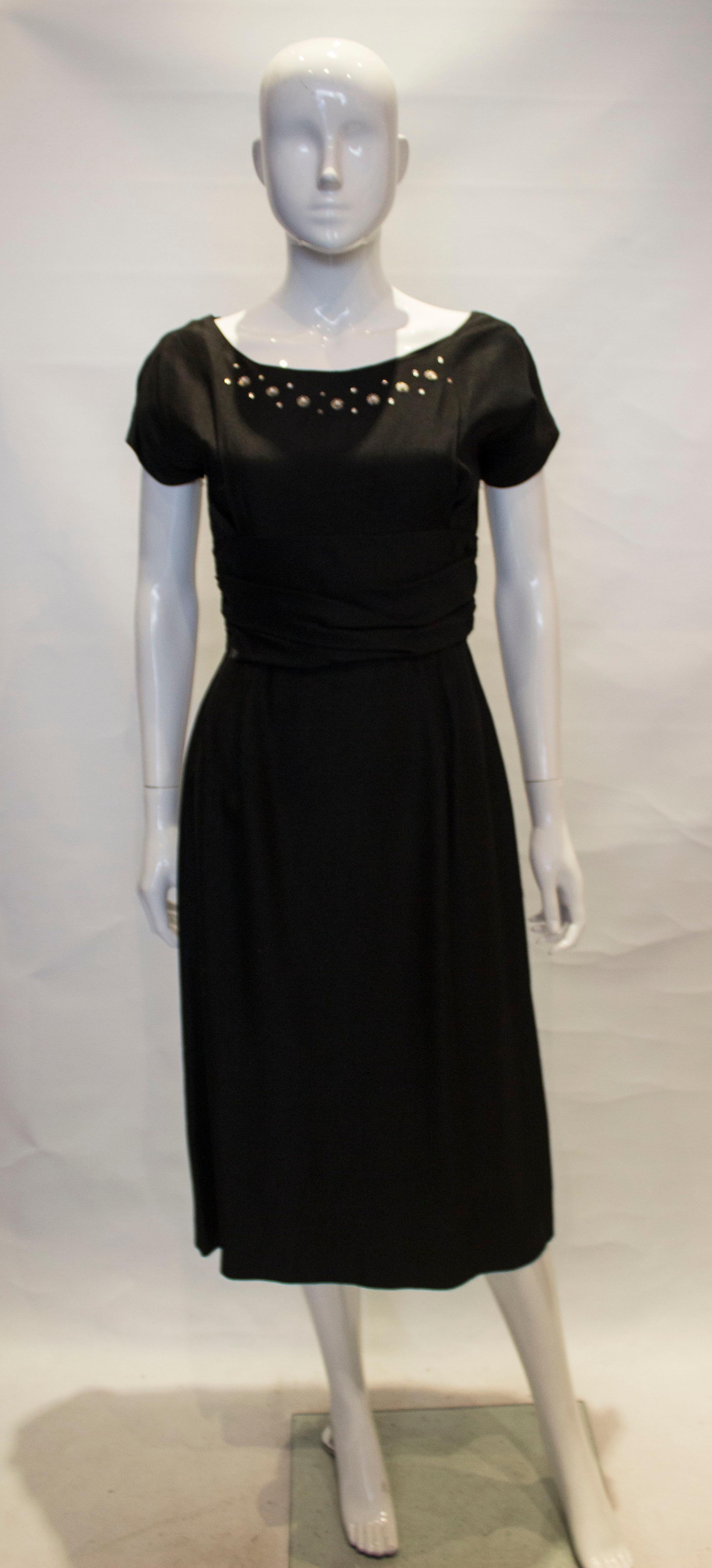 A chic vintage cocktail dress for the festive season. The dress has a boat neckline, with cap sleaves and rouching at the waist. It is marked a size 7 , and has a central back zip.