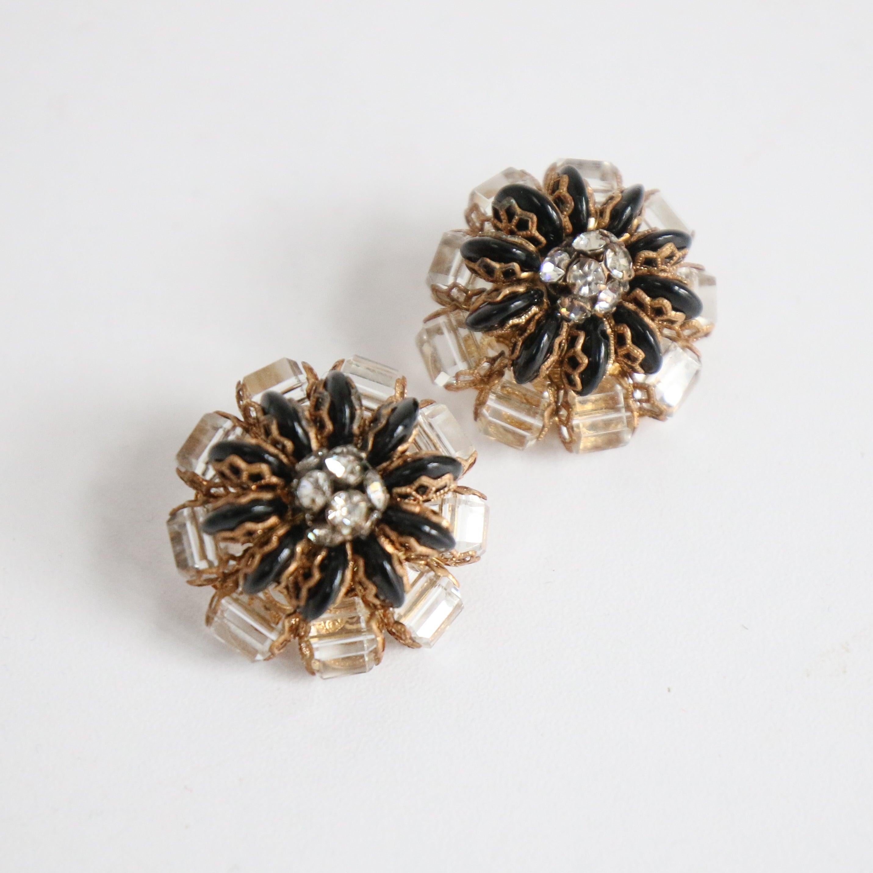 Dieses bezaubernde Paar Ohrclips aus den 1950er Jahren im floralen Design ist mit facettierten, klaren und schwarzen, ovalen Glasperlen mit goldenen Filigranen verziert, die mit einer zentralen Strassperle verziert sind. 

Länge: 1 Zoll

Breite: 1