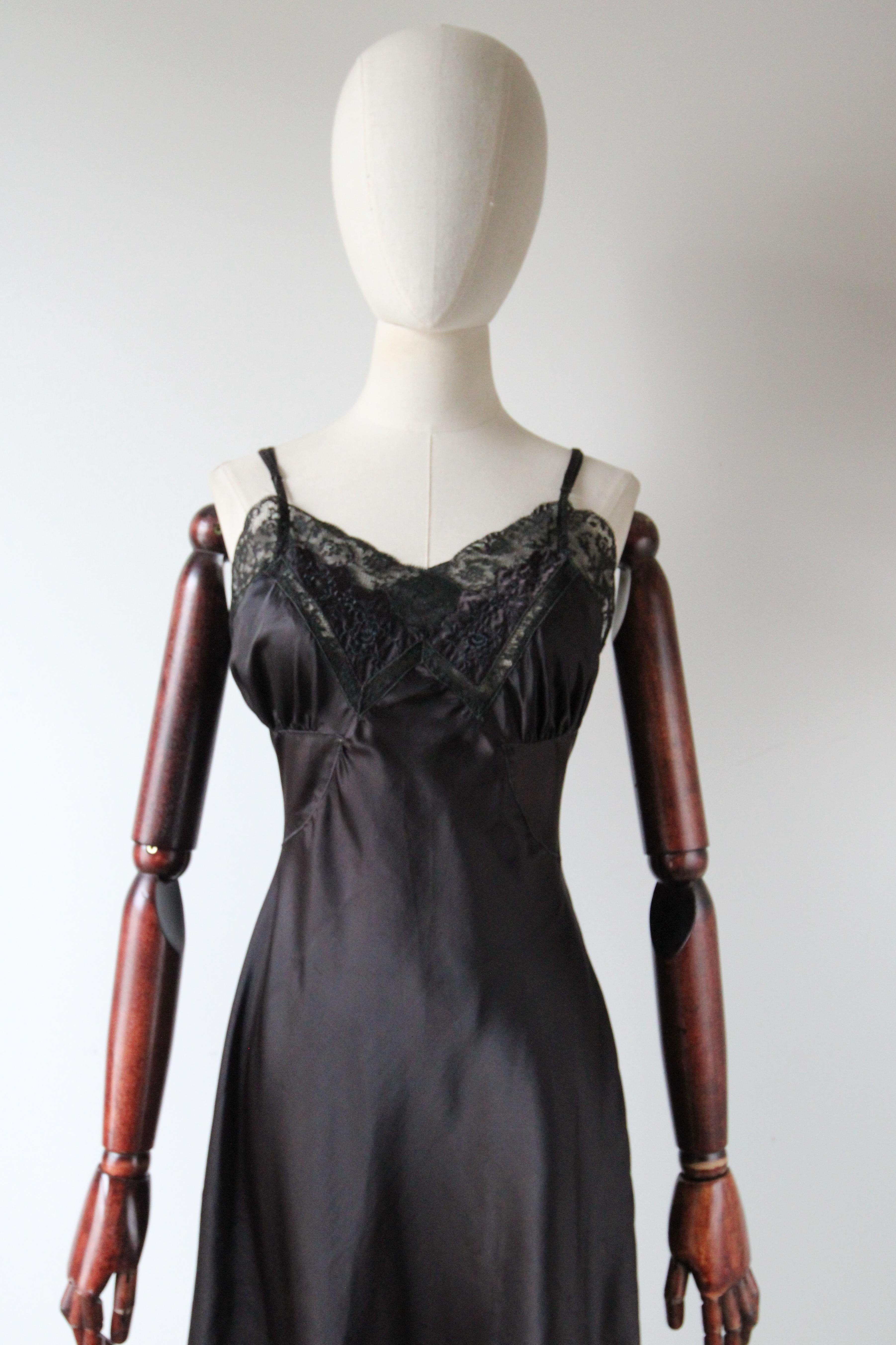 A true staple to every wardrobe, this original 1950's dress slip, rendered in black nylon satin and floral lace, is just the piece for your lingerie collection.  

The scalloped V shaped neckline is edged with black floral lace and framed by