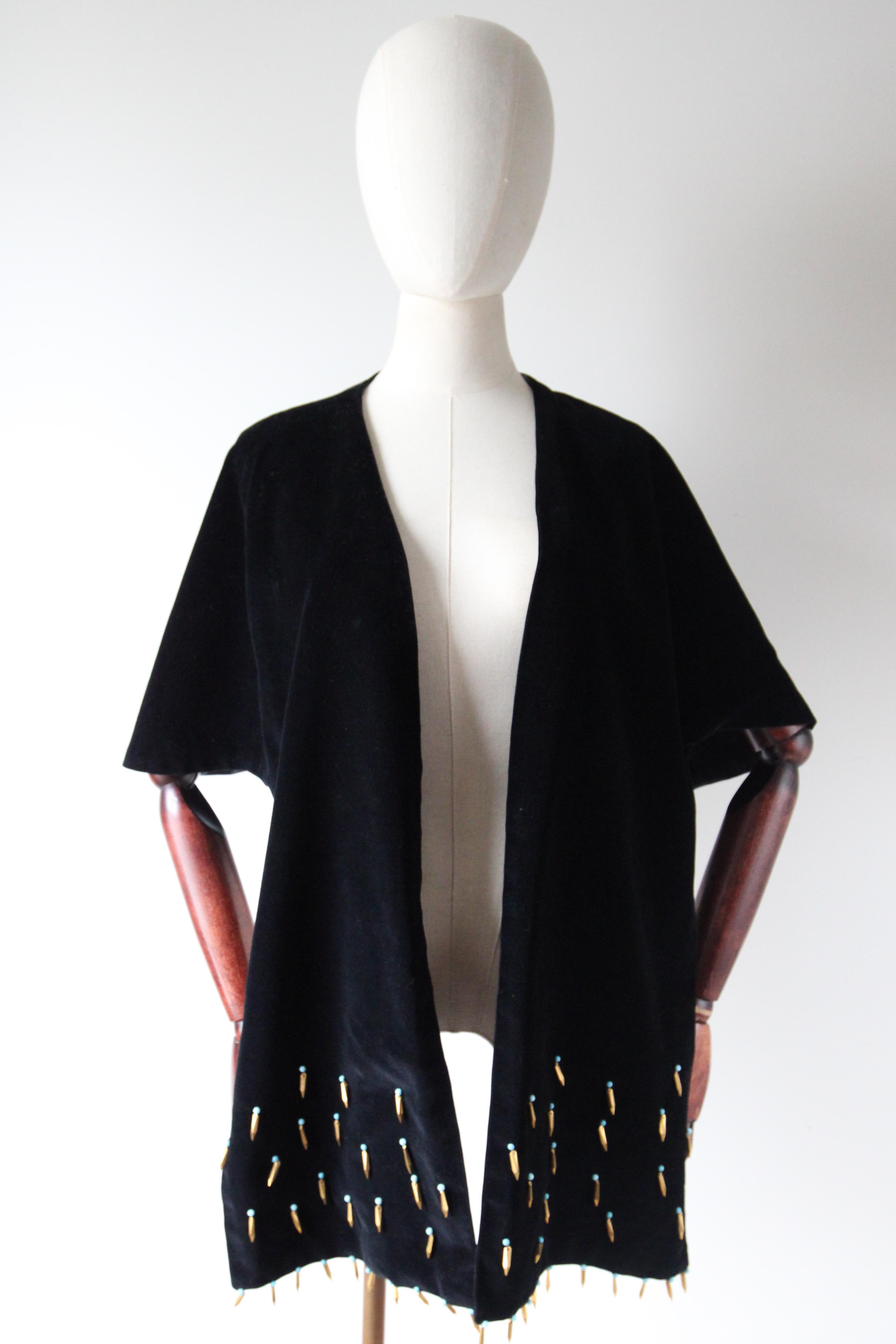 This sumptuous black velvet 1950's evening shawl, adorned with turquoise cabochons and gold toned faceted droplet beads along each extremity, is the perfect finishing touch to your outfit. The elegant capelet cut of the shawl allows for it to sit